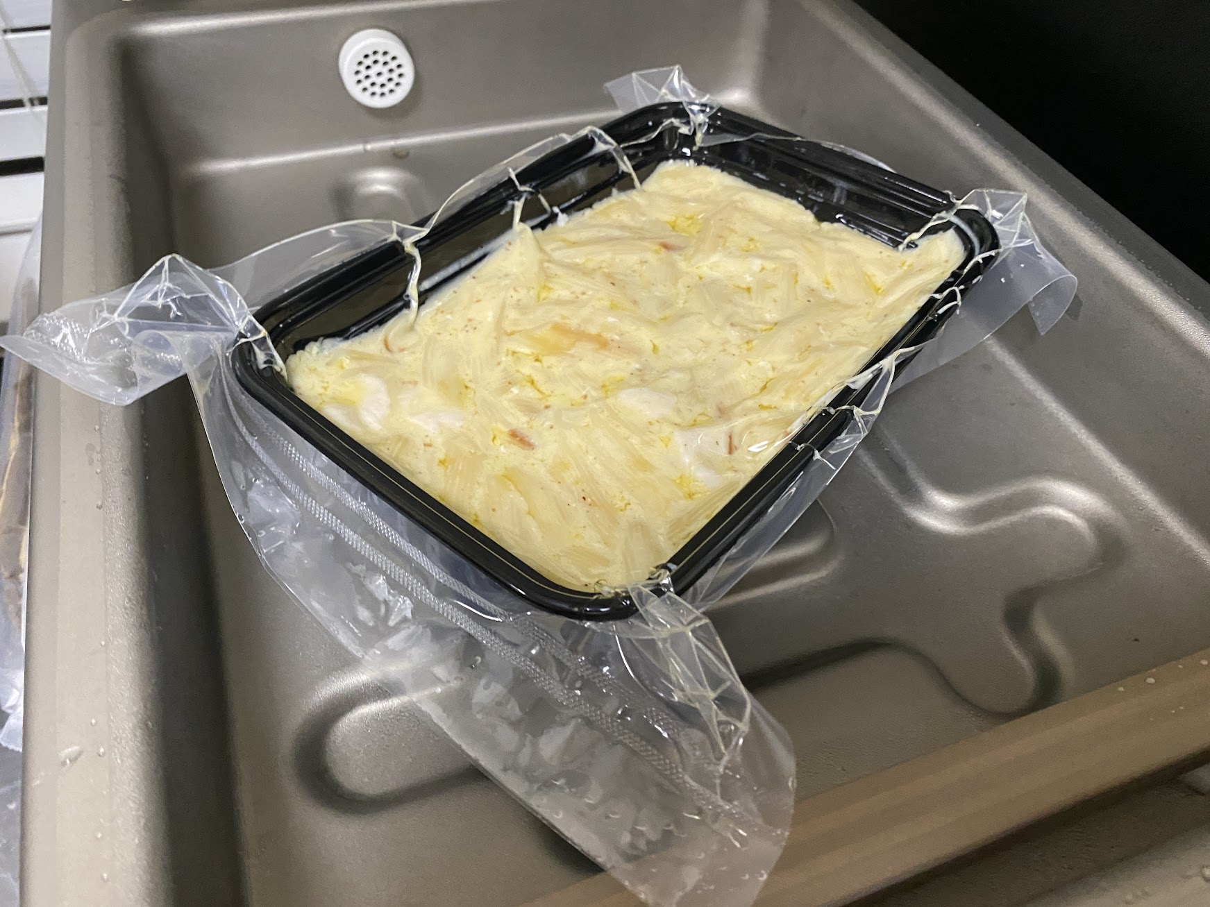 A glass meal prep container filled with leftover Alfredo sauce, sealed with a lid and sitting on a kitchen counter next to a small spoon
