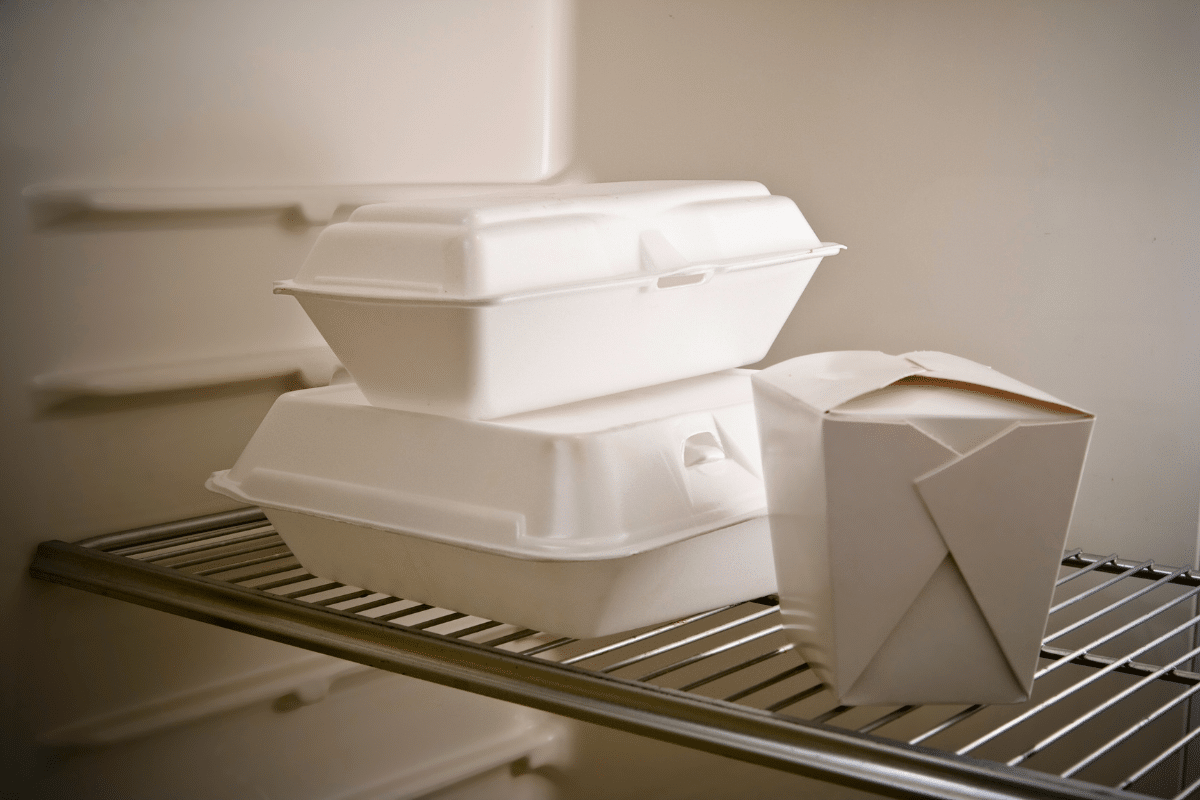 A glass meal prep container filled with leftover Hunan chicken and rice, with the lid set beside it on a kitchen counter