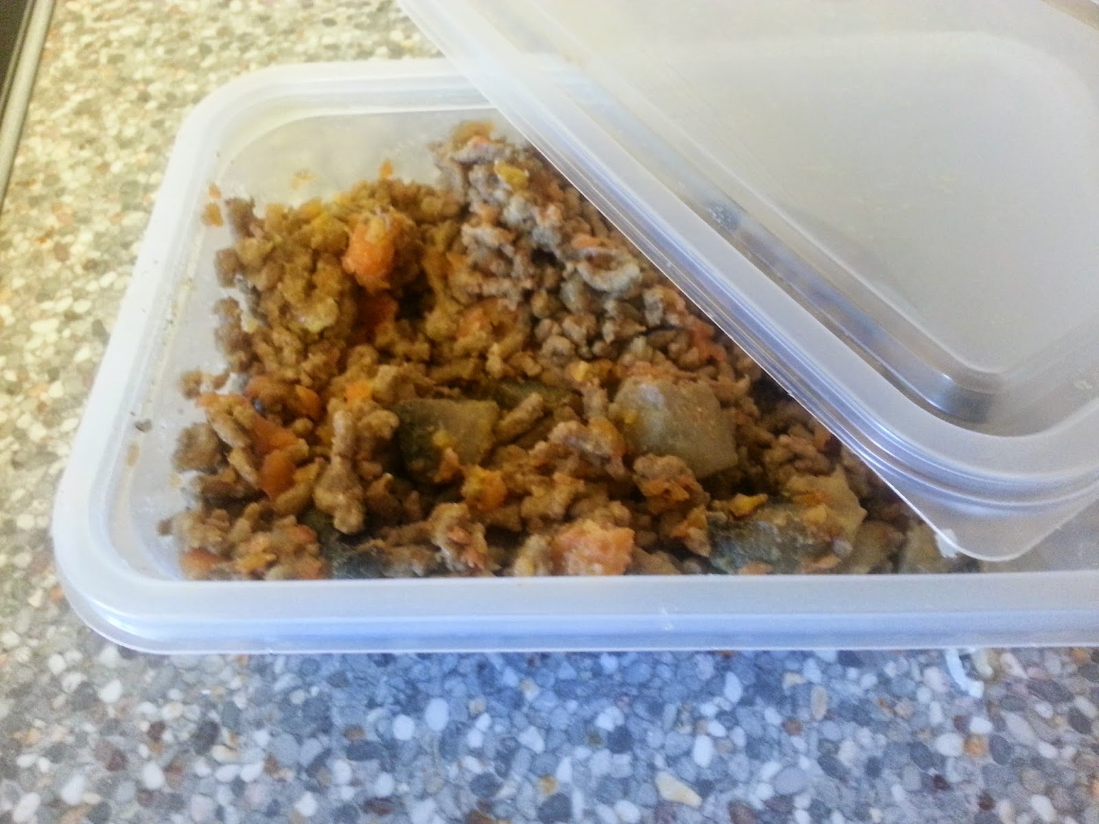 A glass meal prep container filled with leftover bolognese ragù with a lid beside it on a refrigerator shelf