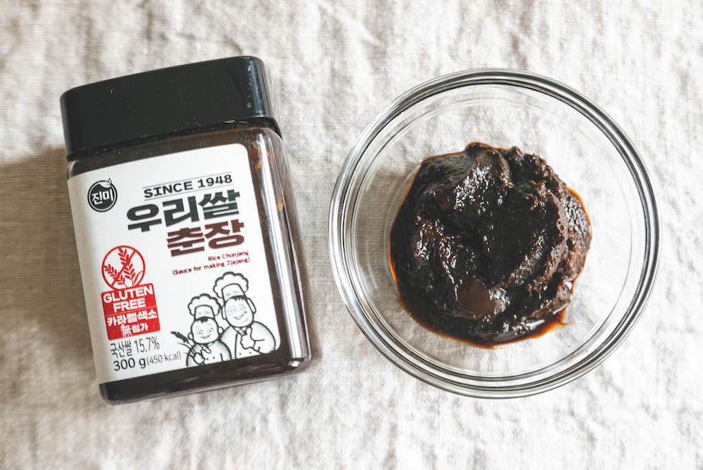 A glass meal prep container filled with leftover black bean sauce cooling on a kitchen counter with a lid nearby