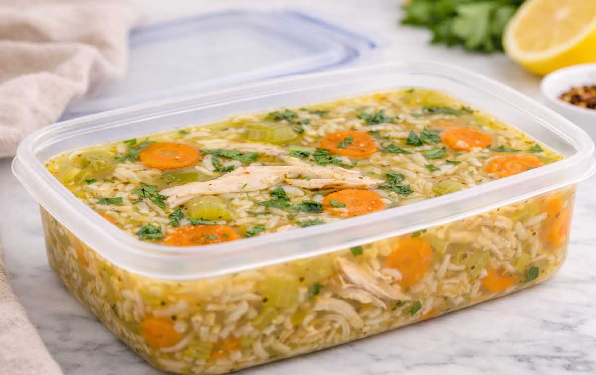 A glass meal prep container filled with leftover chicken and rice with peppers, sitting on a kitchen counter