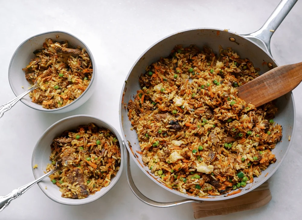 A glass meal prep container filled with leftover chop meat and rice, lid set beside it on a kitchen counter