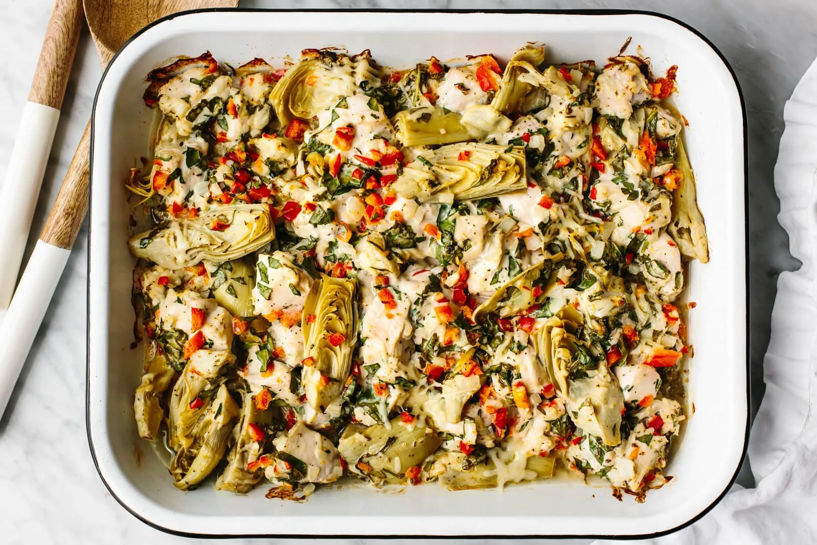 A glass meal prep container filled with leftover creamy chicken and artichokes, covered and sitting on a kitchen counter next to a lemon