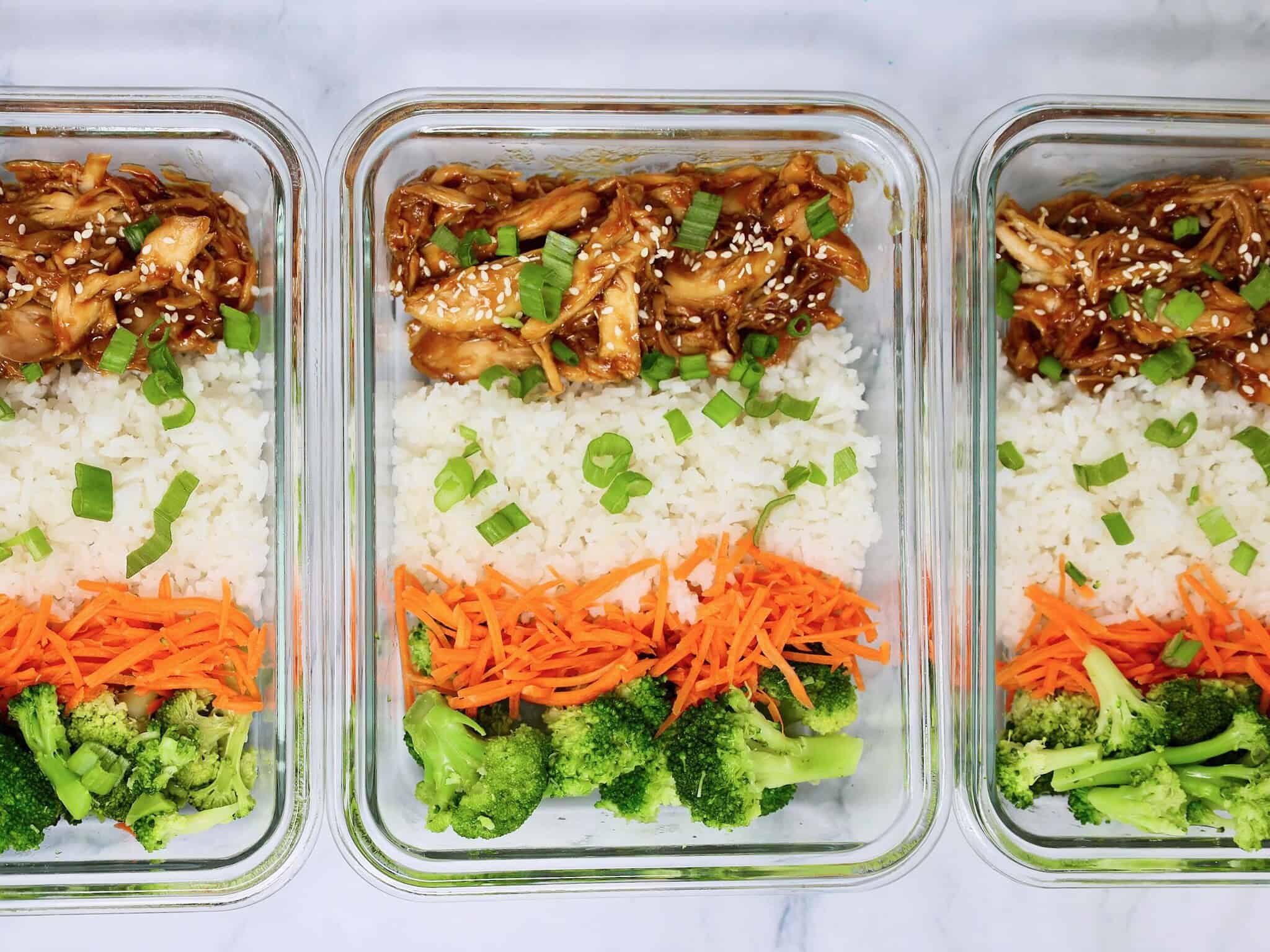 A glass meal prep container filled with leftover lemon garlic chicken and rice, resting on a kitchen counter with a lid nearby
