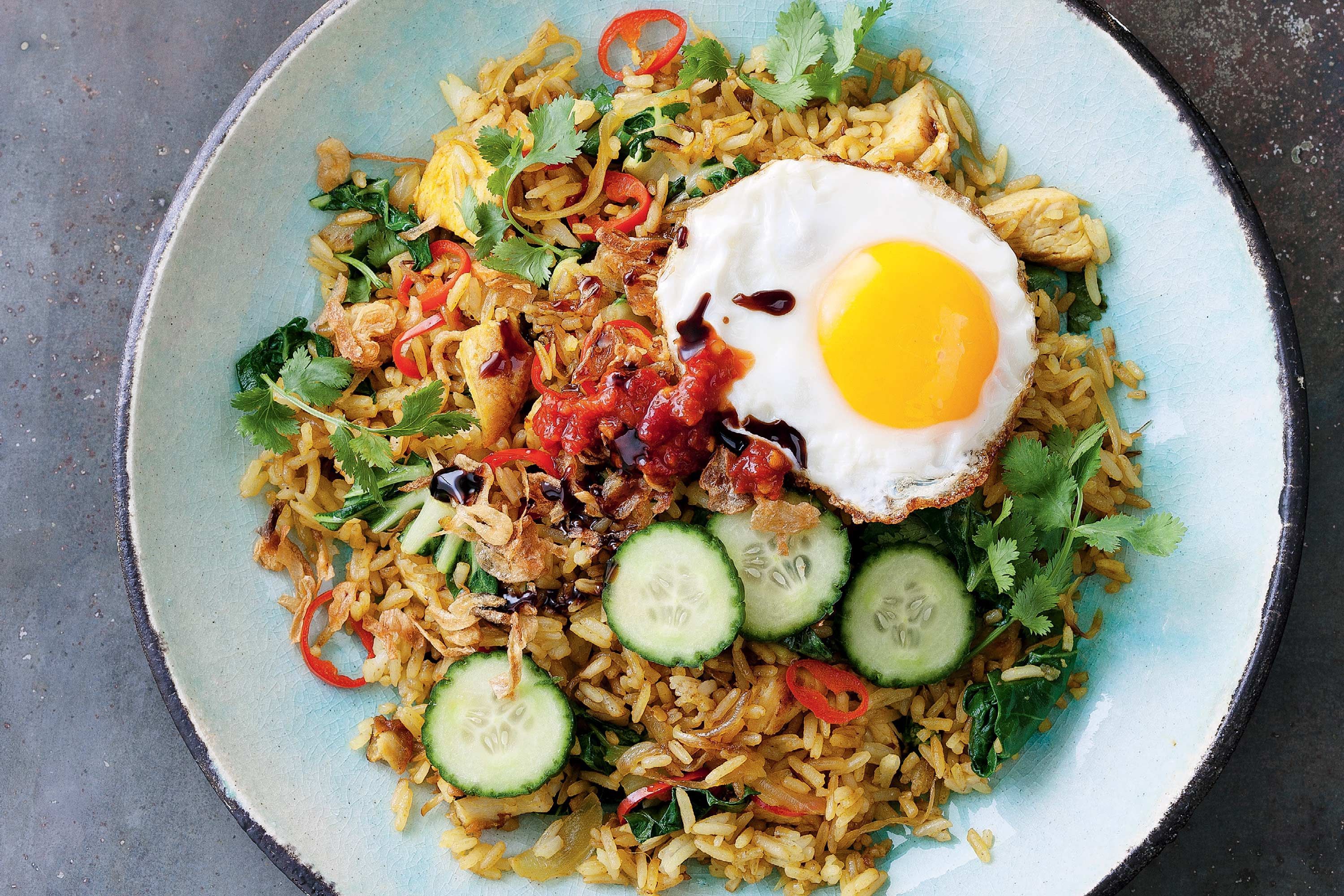 A glass meal prep container filled with leftover nasi goreng on a kitchen counter next to a lidded condiment cup and a lime wedge