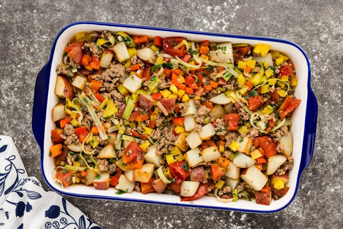 A glass meal prep container filled with leftover roasted sausage, potatoes, peppers, and onions