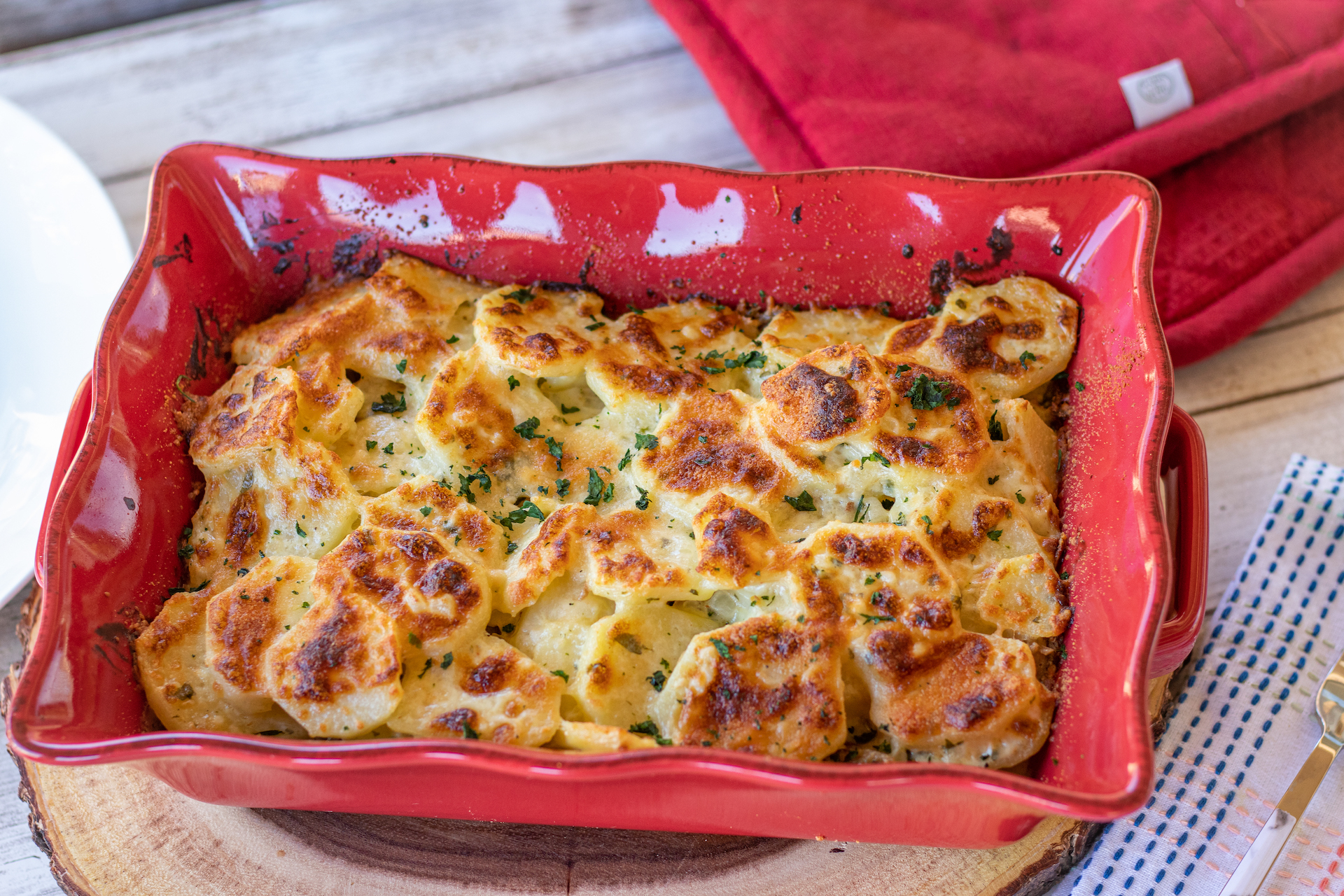 A glass meal prep container filled with leftover scalloped potatoes and ham, lid off on a kitchen counter with a spoon nearby