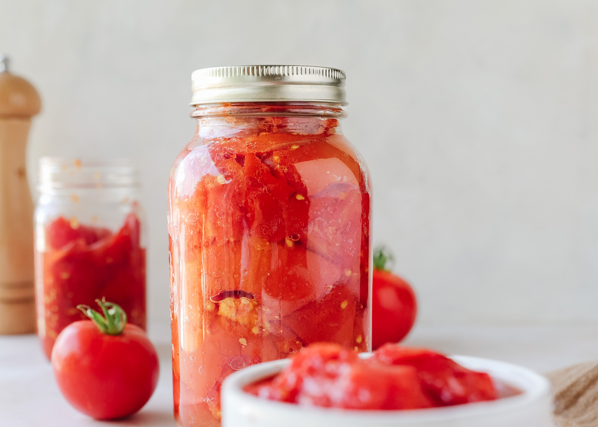 A glass meal prep container filled with leftover stewed tomatoes cooling on a kitchen counter with the lid set beside it