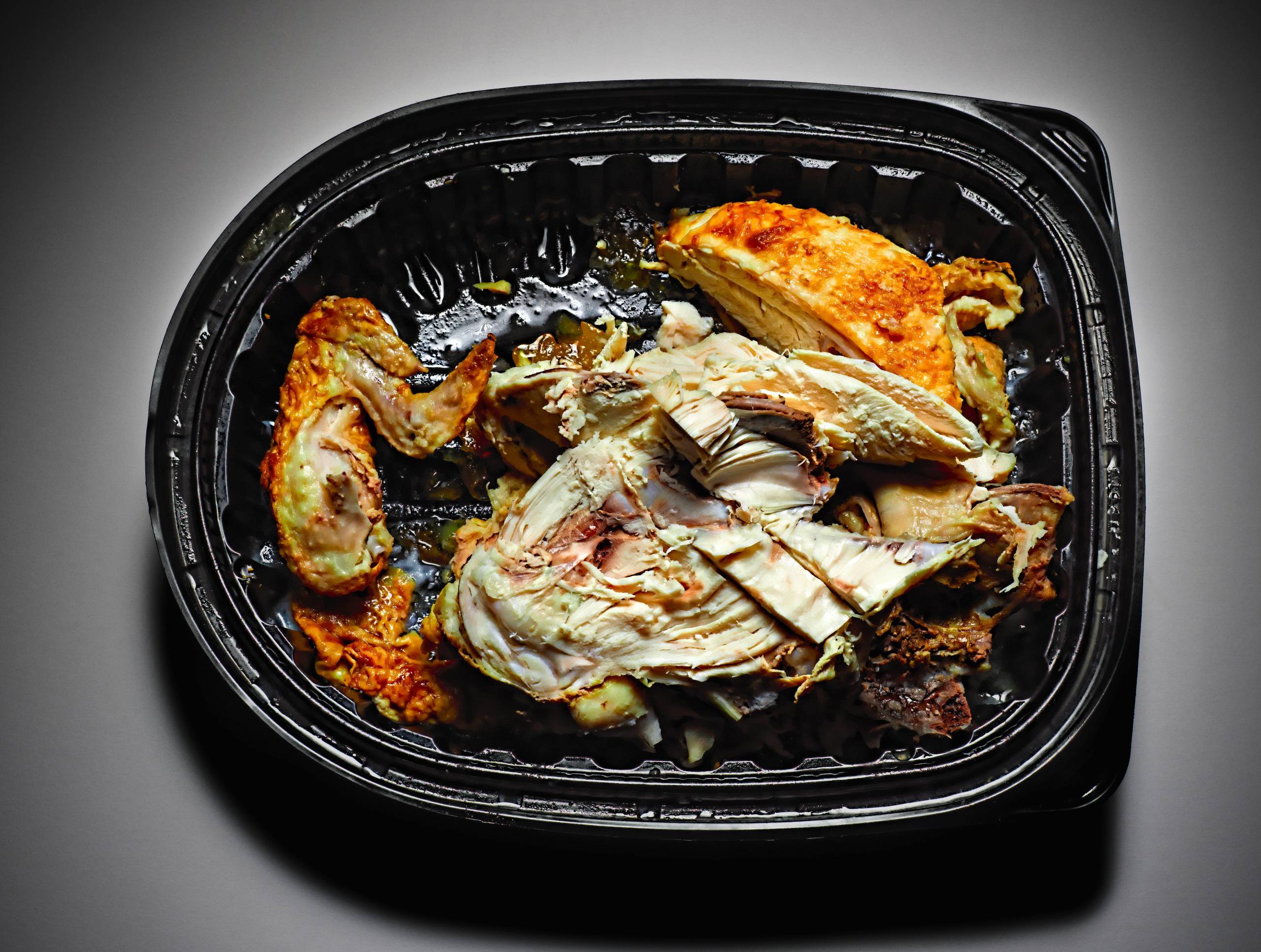 A glass meal prep container filled with leftover stewed chicken and vegetables, lid set beside it on a kitchen counter