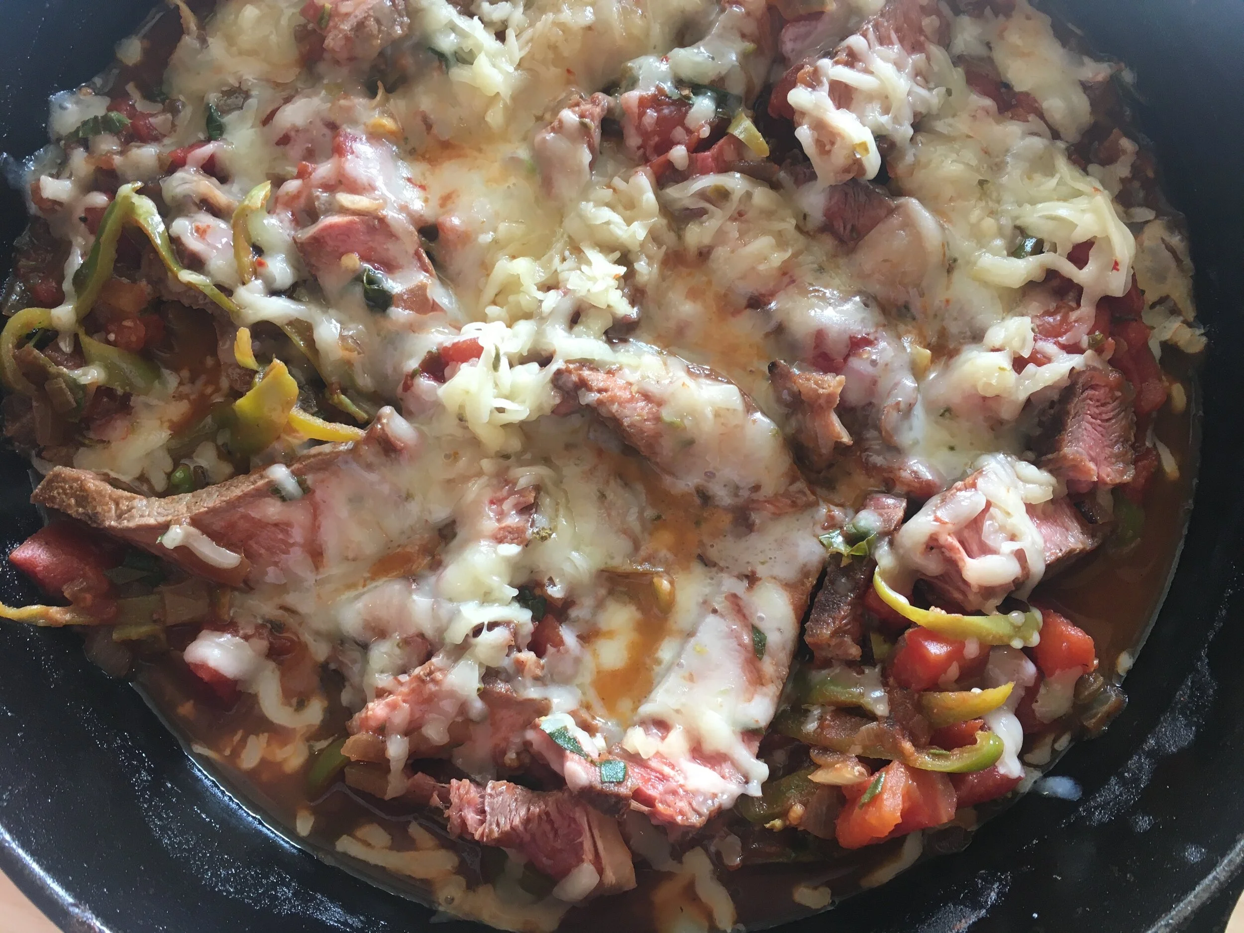 A glass meal prep container filled with leftover steak pizzaiola in tomato sauce, lid resting beside it on a kitchen counter