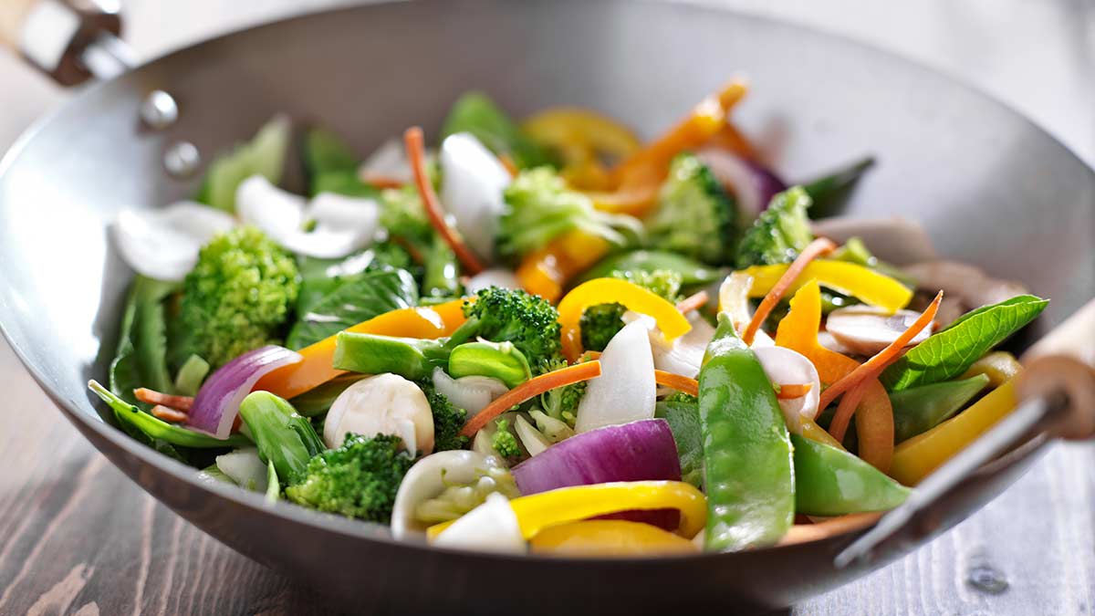 A glass meal prep container filled with leftover vegetable stir-fry and rice on a kitchen counter with a lid nearby