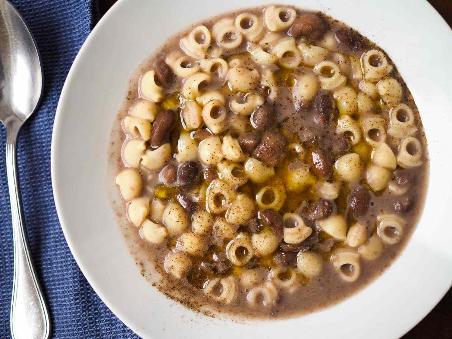 A glass meal prep container filled with pasta e fagioli, with a small container of cooked ditalini beside it on a kitchen counter