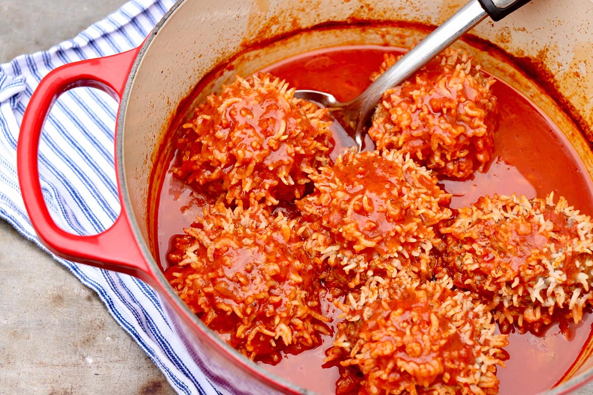 A glass meal prep container filled with porcupine meatballs and tomato sauce, lid set nearby on a kitchen counter