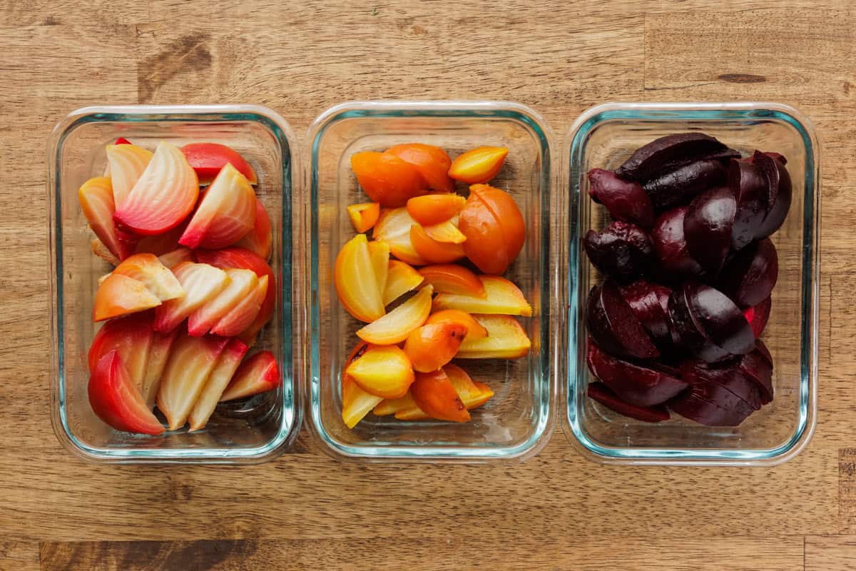 A glass meal prep container filled with roasted beetroot wedges, lid set nearby on a clean kitchen counter