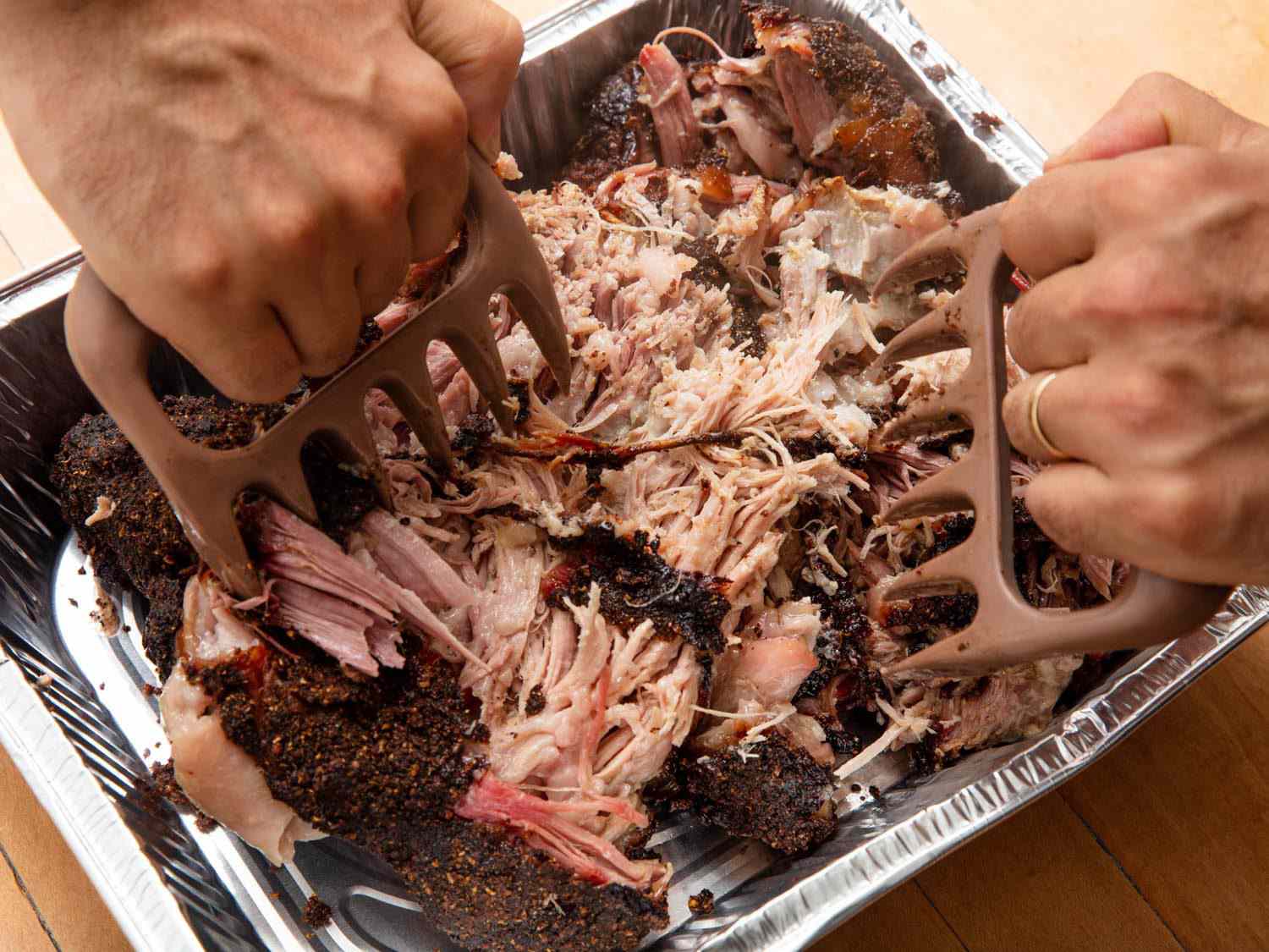 A glass meal prep container filled with shredded pork roast, carrots, potatoes, and gravy on a kitchen counter next to a lid