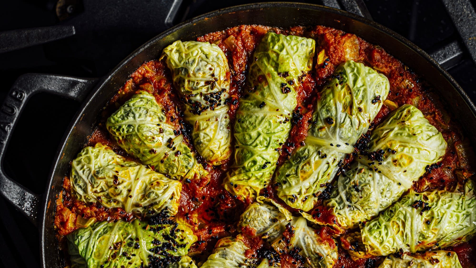 A glass meal prep container filled with two cabbage rolls covered in tomato sauce, lid set beside it on a kitchen counter