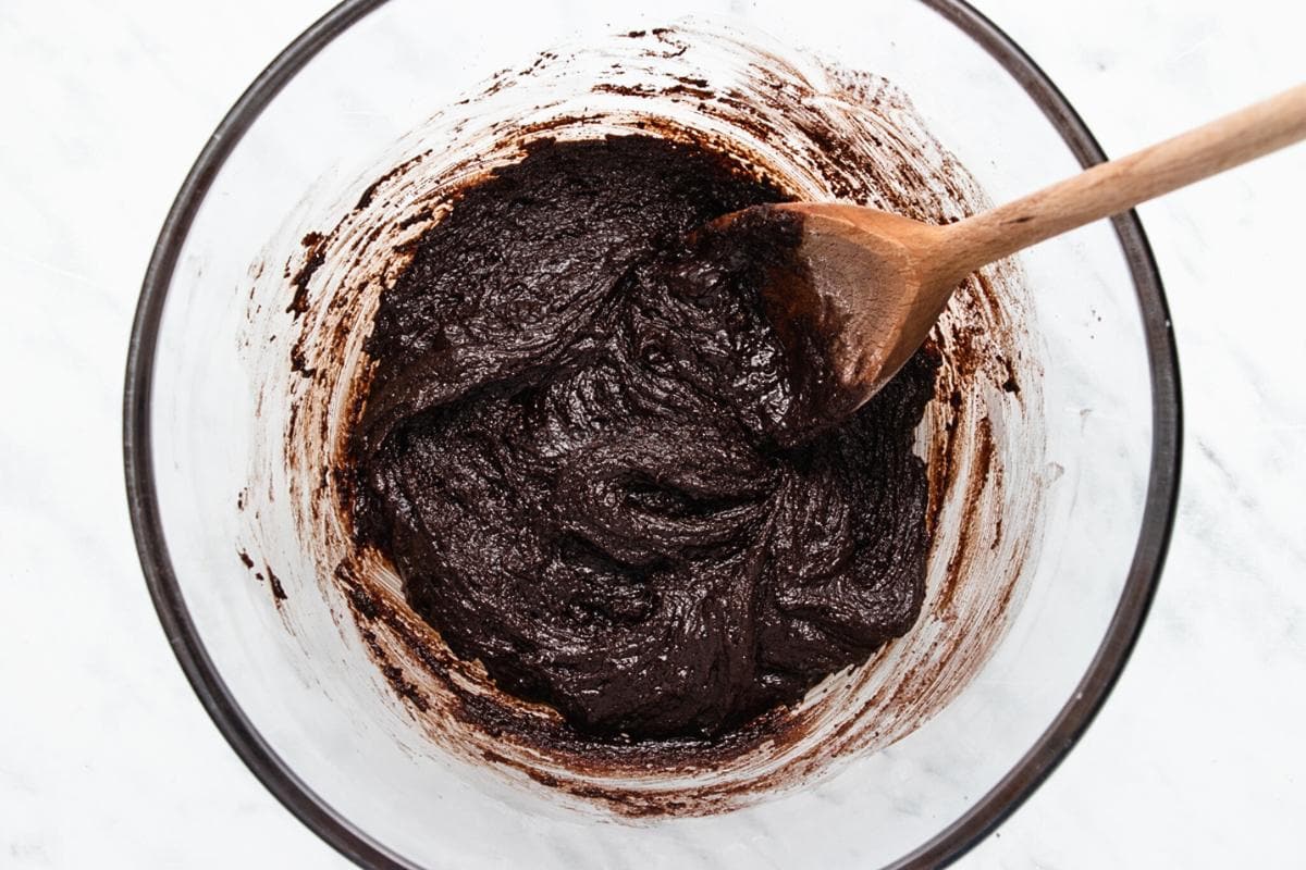 A glass mixing bowl filled with thick chocolate brownie batter