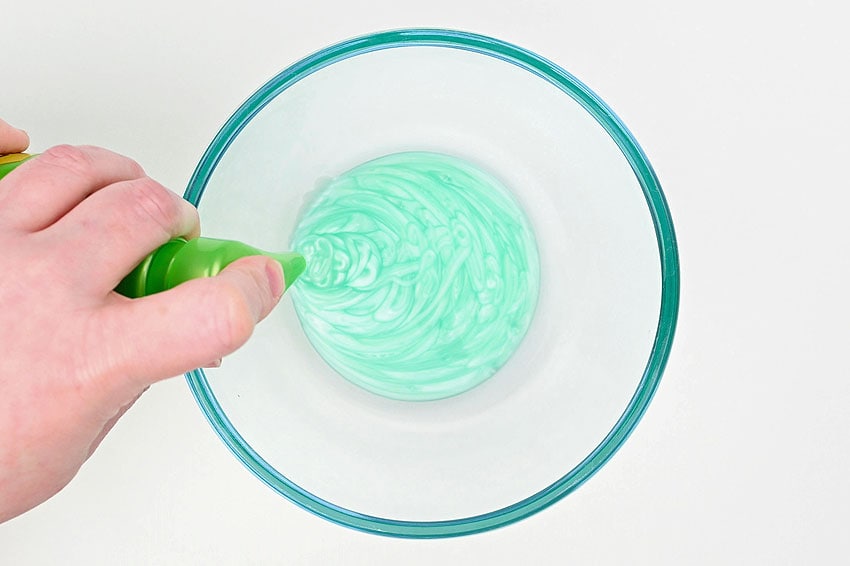 A glass mixing bowl of pale pastel no-glue slime on a bright kitchen counter, with a spoon and small bowls of cornstarch nearby