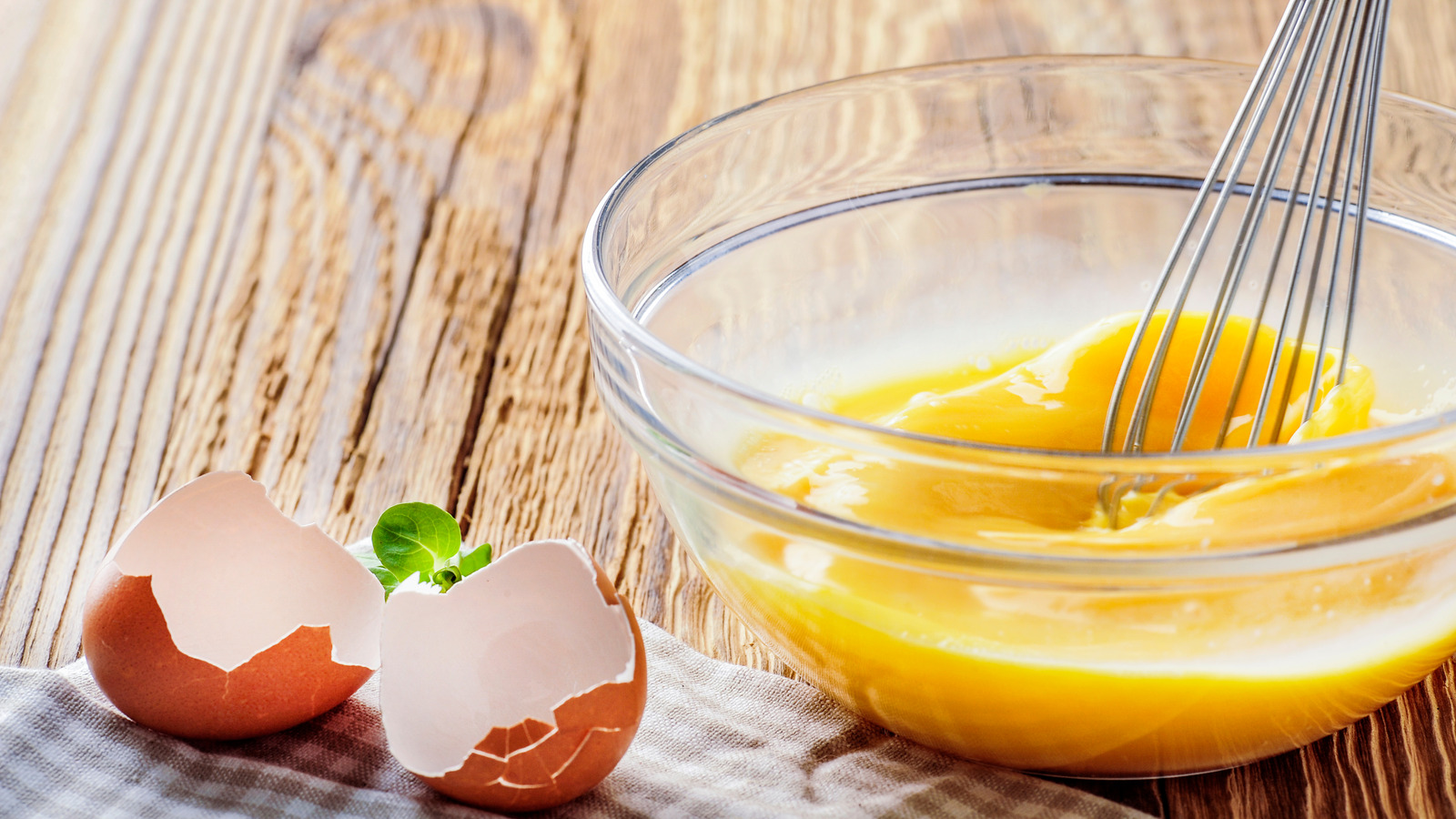 A glass mixing bowl of whisked-eggs on a kitchen counter with a whisk resting inside, soft afternoon light