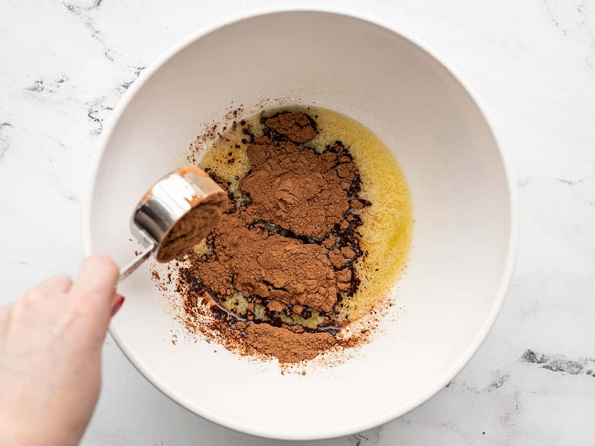 A glass mixing bowl on a kitchen counter with warm melted butter being whisked together with cocoa powder until glossy