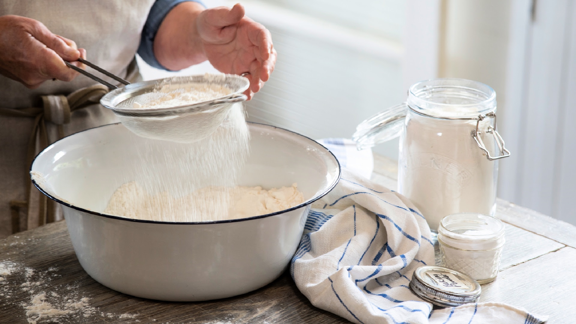 A glass mixing bowl with flour, baking powder, salt, and sugar measured out on a bright kitchen counter