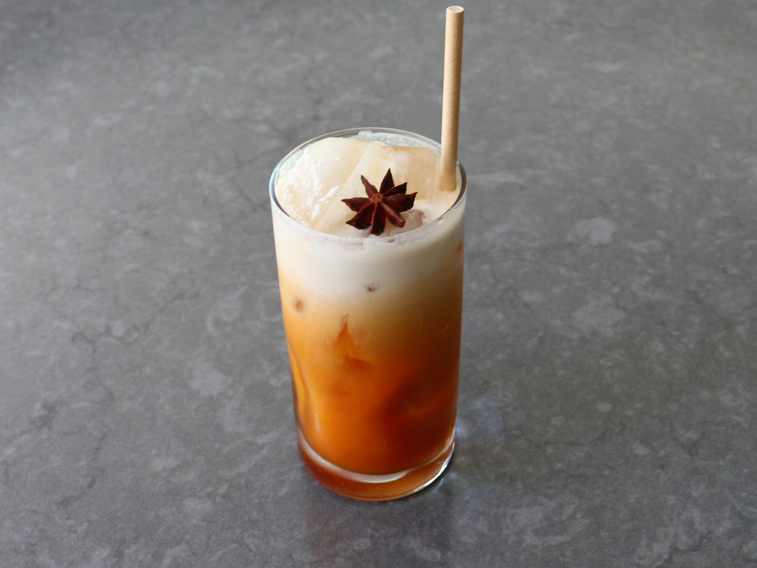 A glass of Thai iced tea with visible layers of tea and cream over ice, condensation on the glass, photorealistic food photography