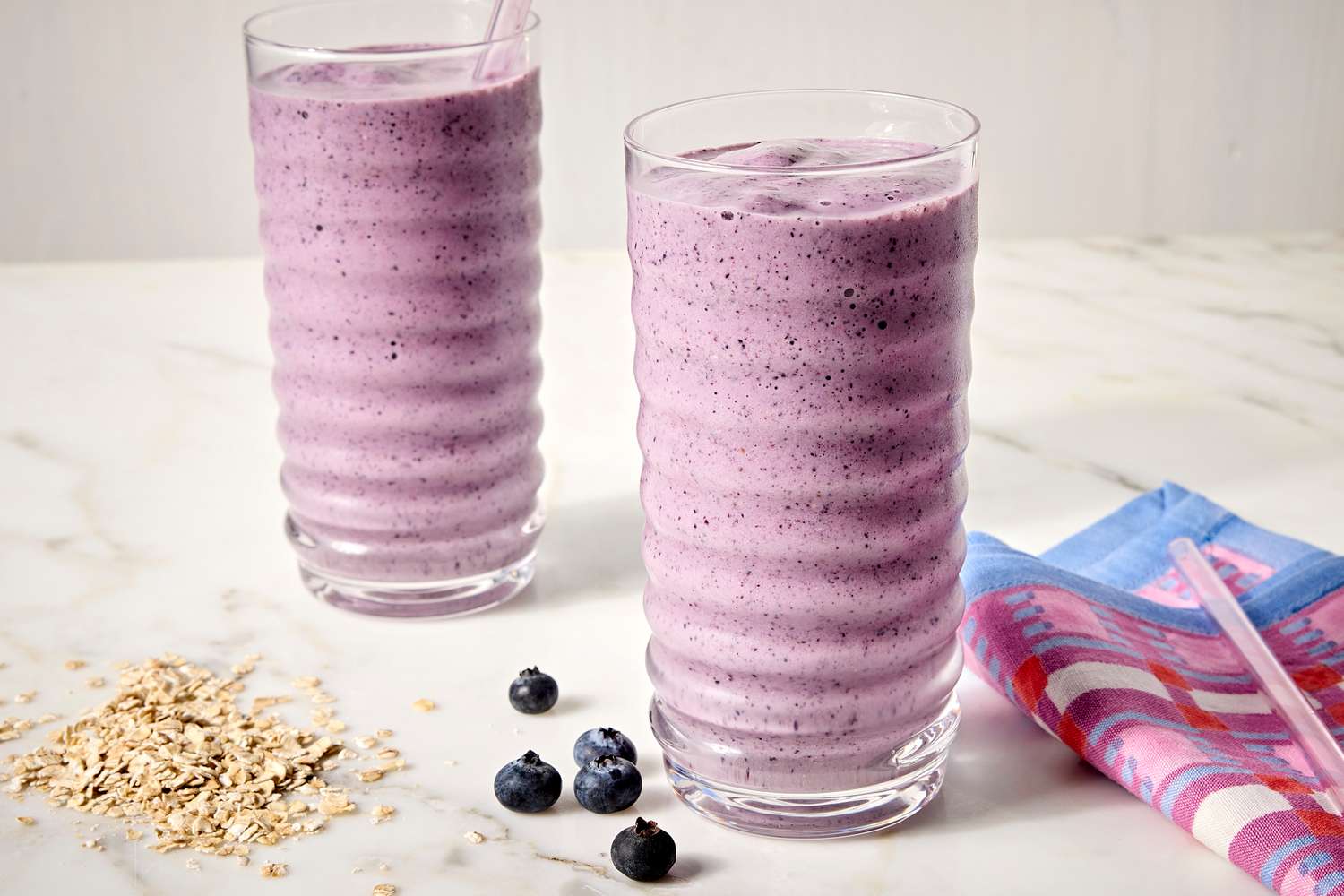 A glass of thick berry oat smoothie on a light stone kitchen counter with fresh berries and a spoon nearby, soft morning window light