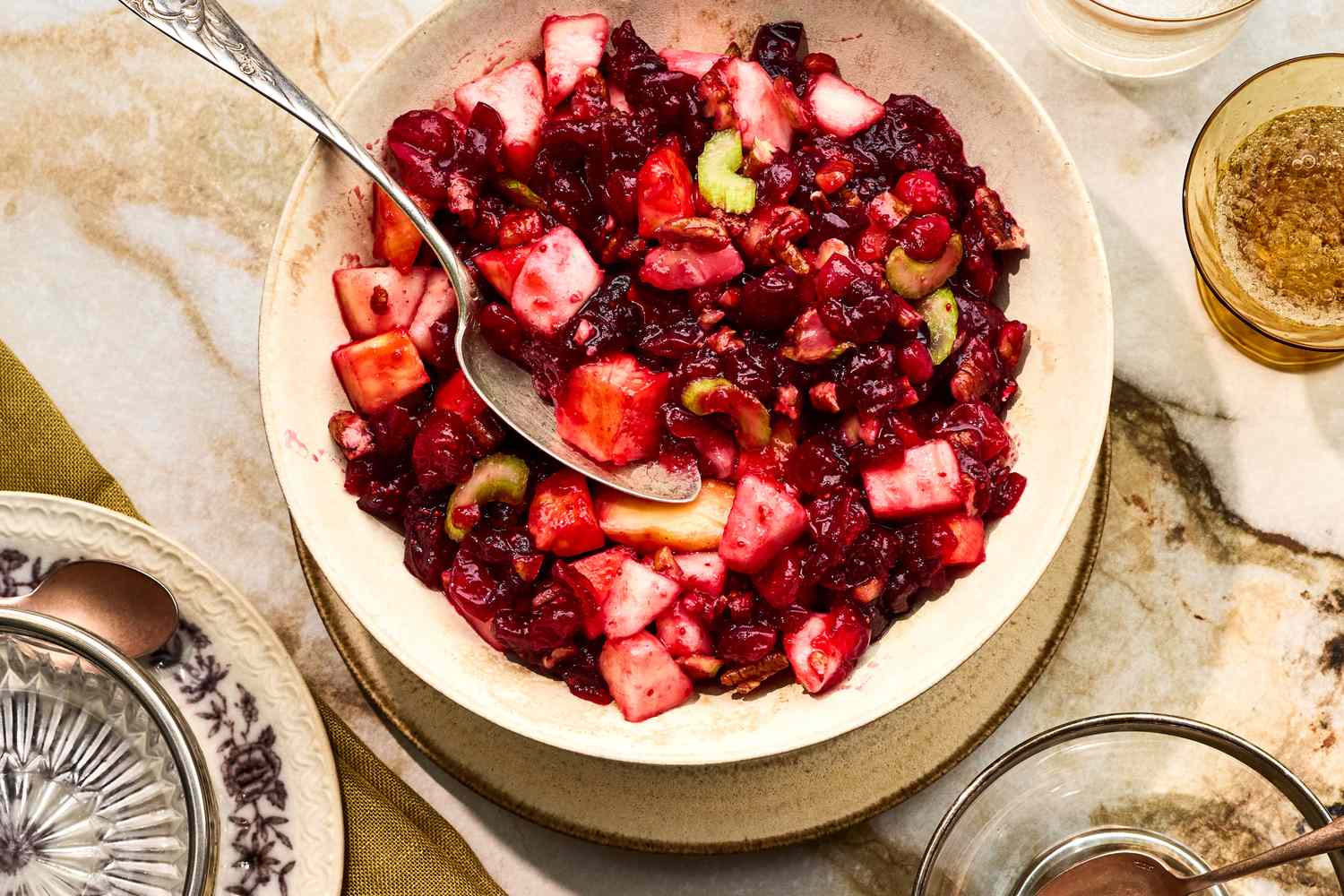 A glass serving bowl filled with creamy cranberry salad studded with chopped cranberries and pineapple, topped with a sprinkle of chopped pecans on a rustic kitchen table