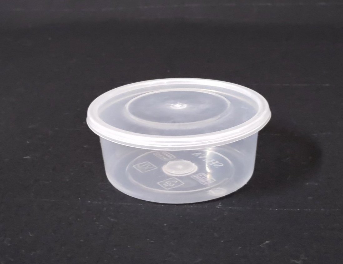 A glass storage container filled with cucumber raita on a refrigerator shelf, lid set nearby