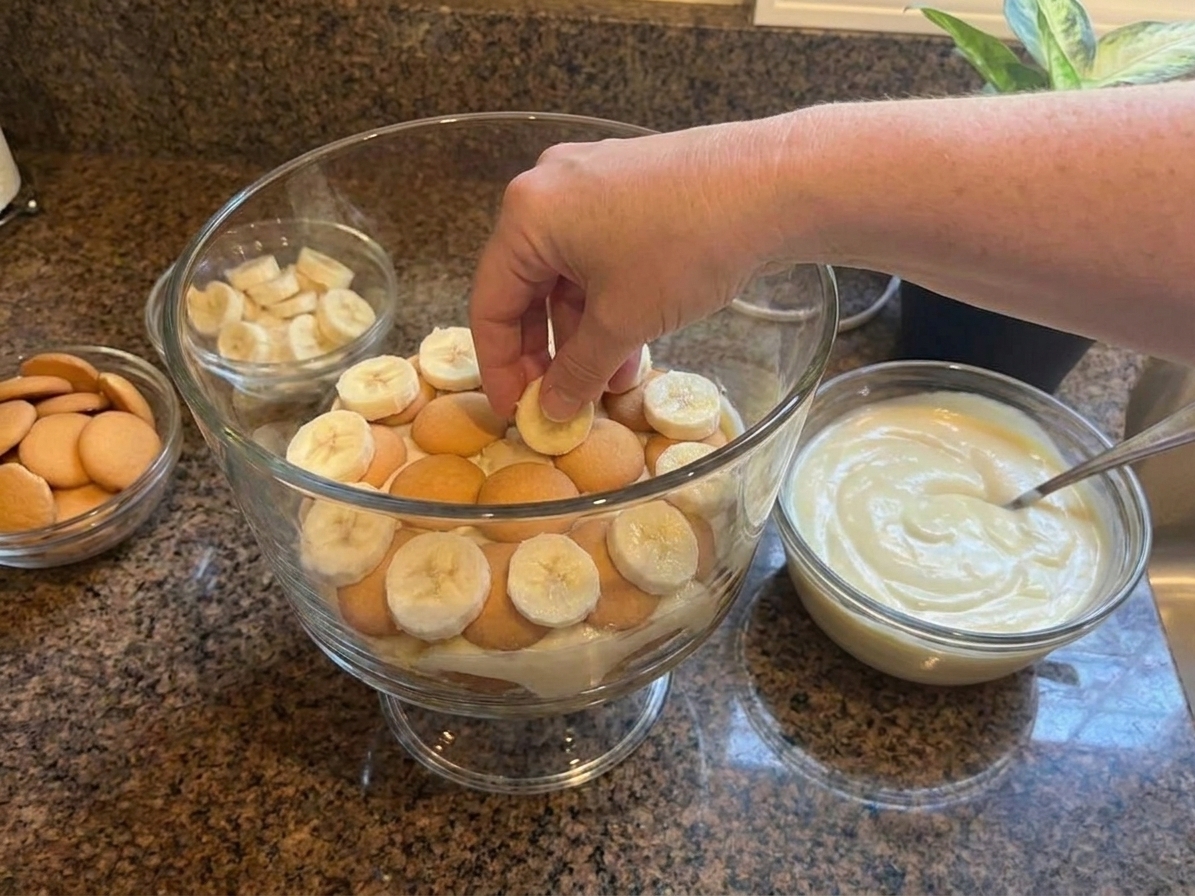 A glass trifle dish filled with layers of creamy banana pudding, sliced bananas, and vanilla wafers on a bright kitchen counter