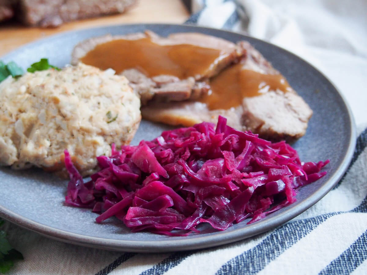 A glossy bowl of German braised red cabbage with tender apple pieces on a rustic table setting, warm kitchen lighting