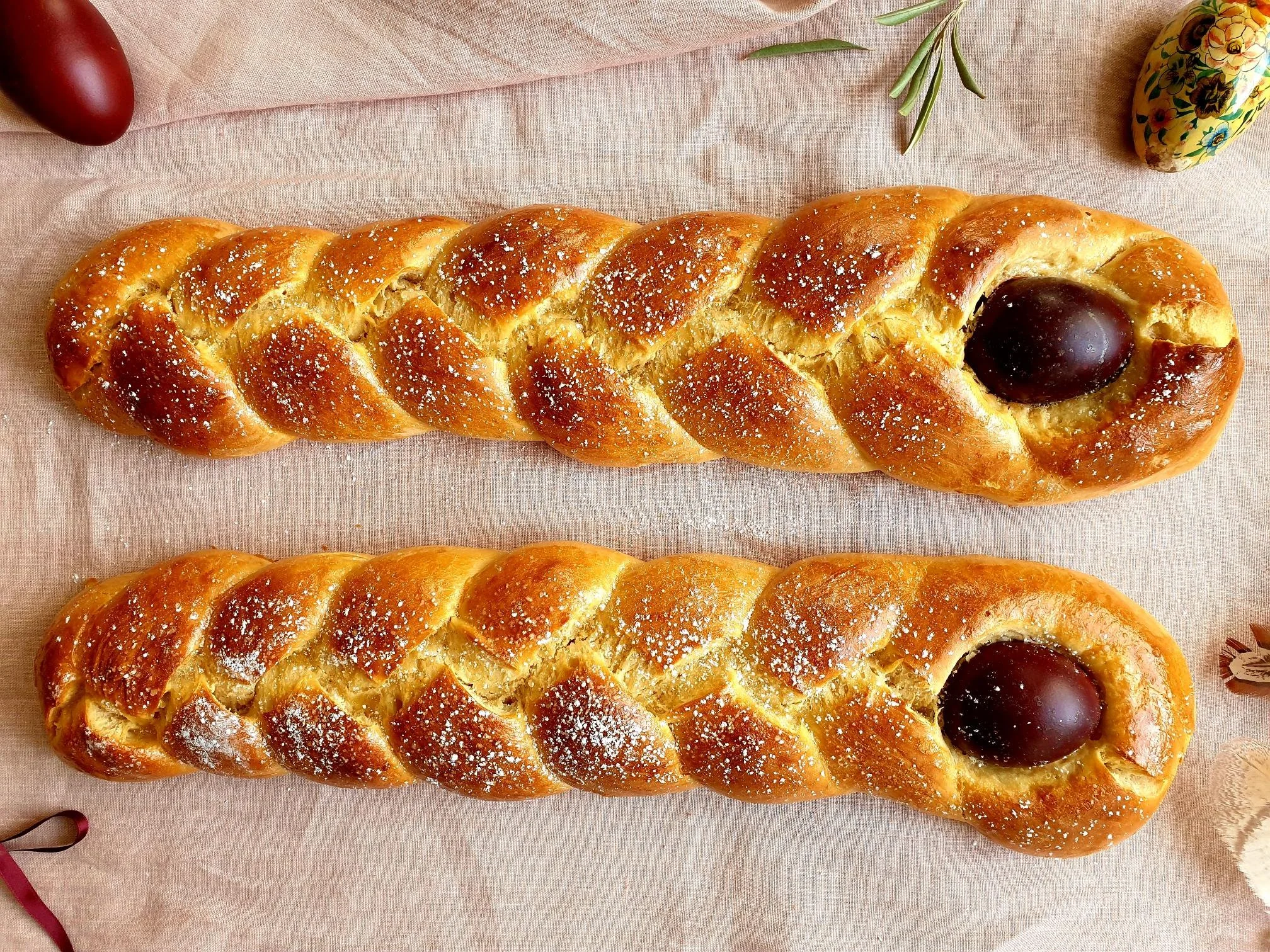 A glossy braided Easter bread loaf on a parchment-lined baking sheet on a warm kitchen counter, golden brown crust with pearl sugar, soft natural window light