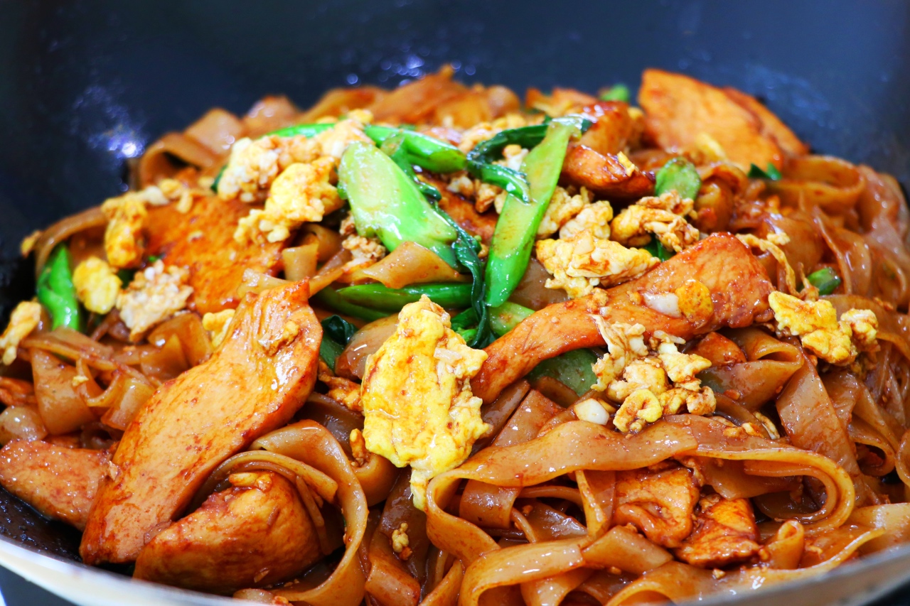 A glossy plate of pad see ew with wide rice noodles, Chinese broccoli, and scrambled egg, with lightly charred edges on a simple dinner table