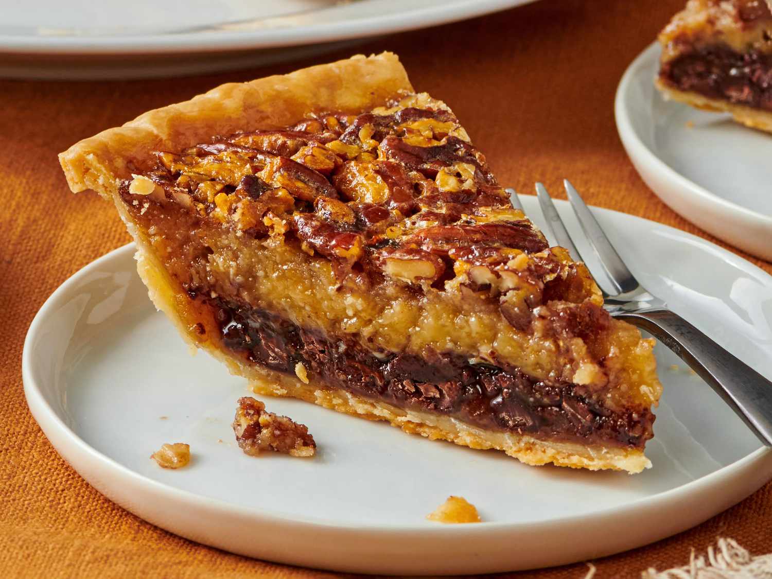 A glossy slice of chocolate pecan pie on a dessert plate, showing a gooey chocolate filling with toasted pecans on top