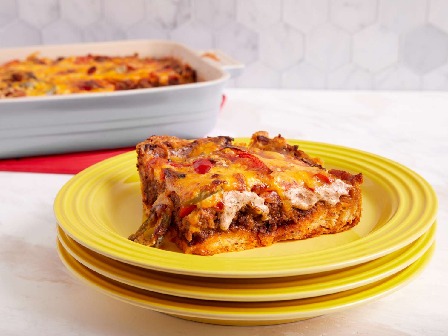 A golden baked John Wayne casserole in a glass baking dish on a light kitchen counter, with bubbling cheese on top and a serving spoon nearby