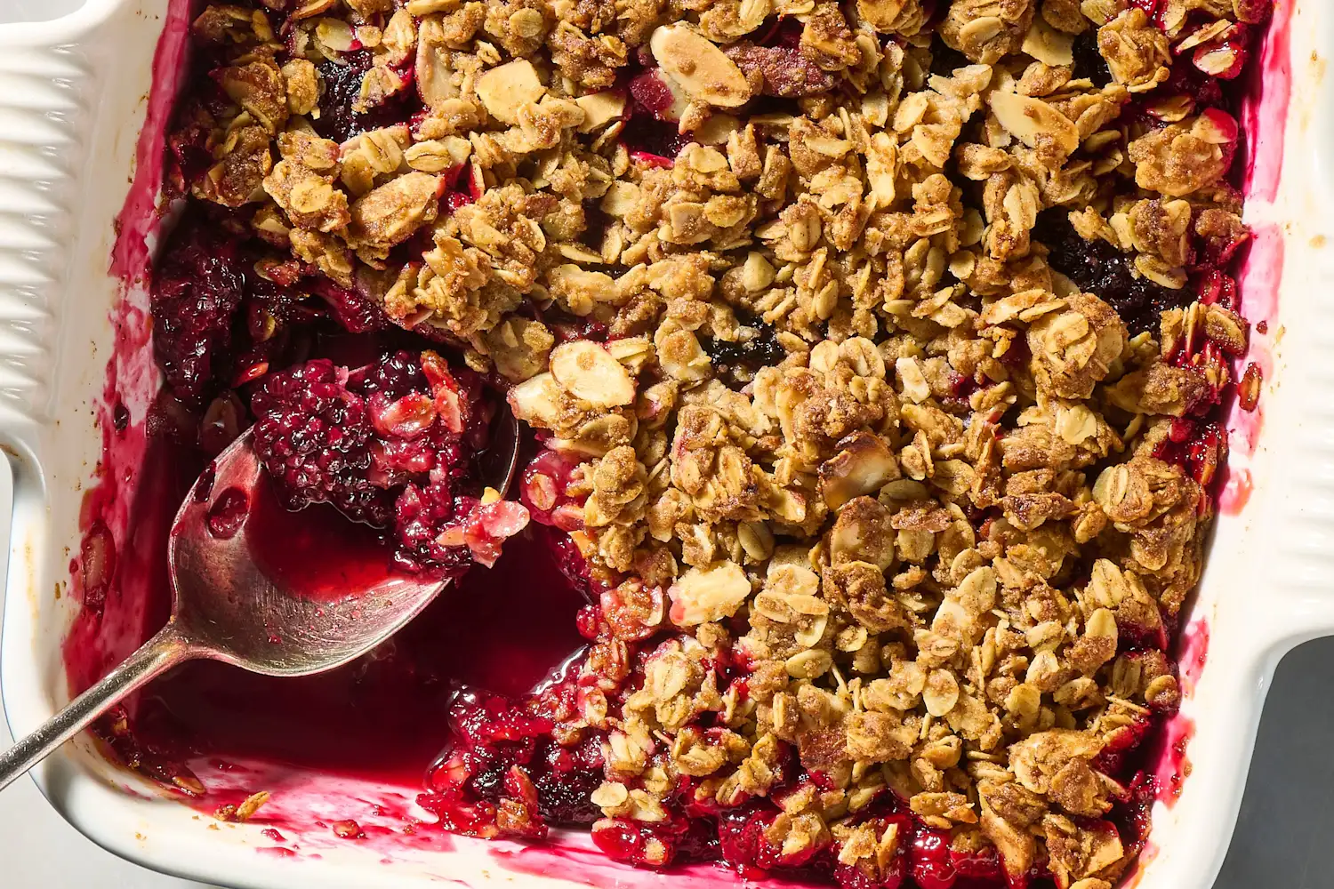 A golden baked blackberry crisp in a square baking dish with bubbling purple juices around the edges on a warm kitchen counter