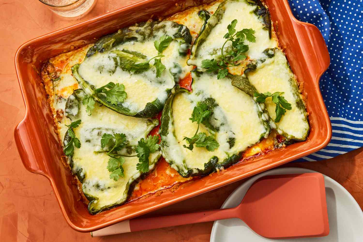 A golden baked chile relleno casserole in a white ceramic baking dish on a neutral kitchen counter, with bubbly browned cheese and sliced green chiles visible on top