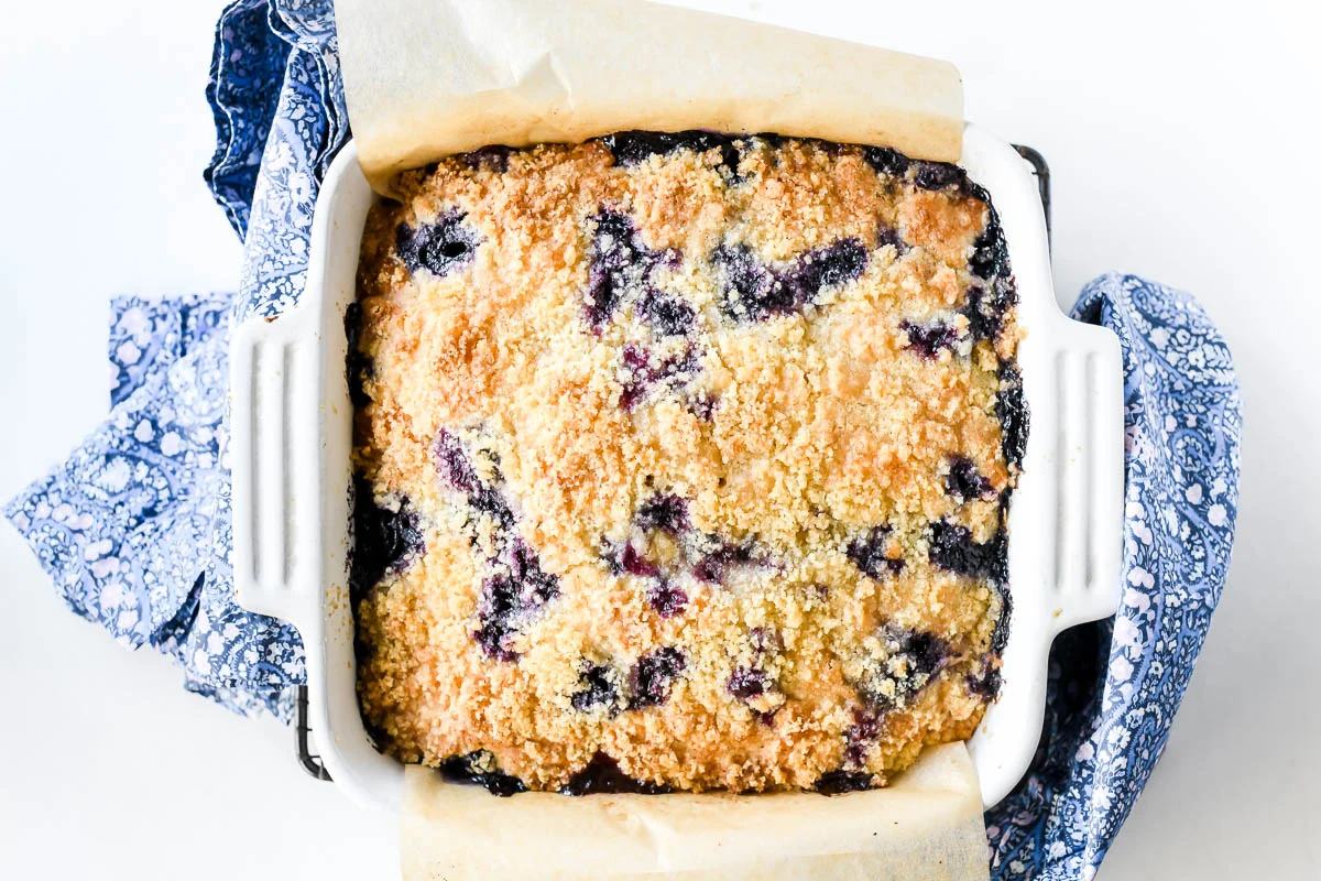 A golden blueberry buckle in a square baking pan with a crisp cinnamon streusel topping and visible blueberries