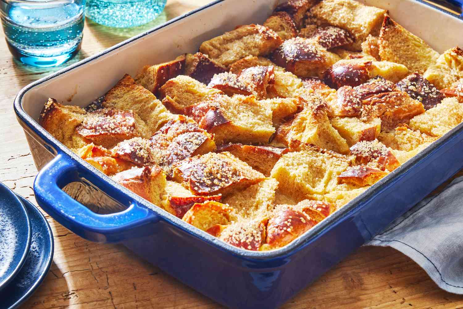 A golden brown bread pudding fresh from the oven in a ceramic baking dish with crisp edges and a custardy center, real food photography