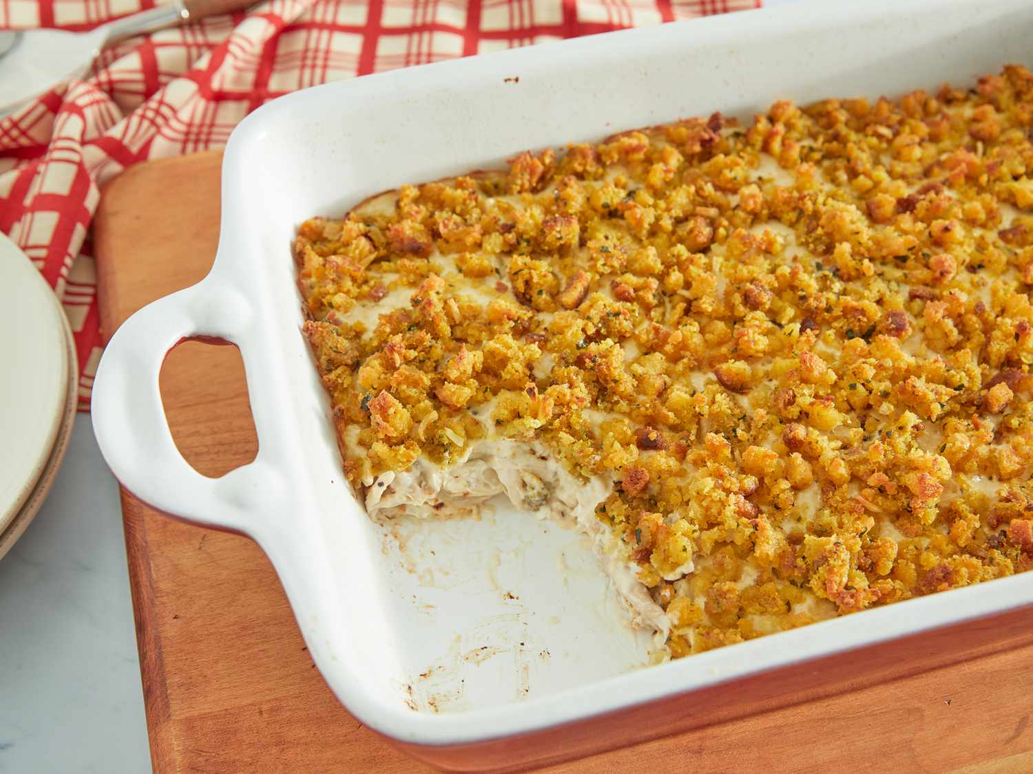 A golden-brown chicken and stuffing casserole in a white ceramic baking dish on a light kitchen counter, with a serving spoon resting beside it