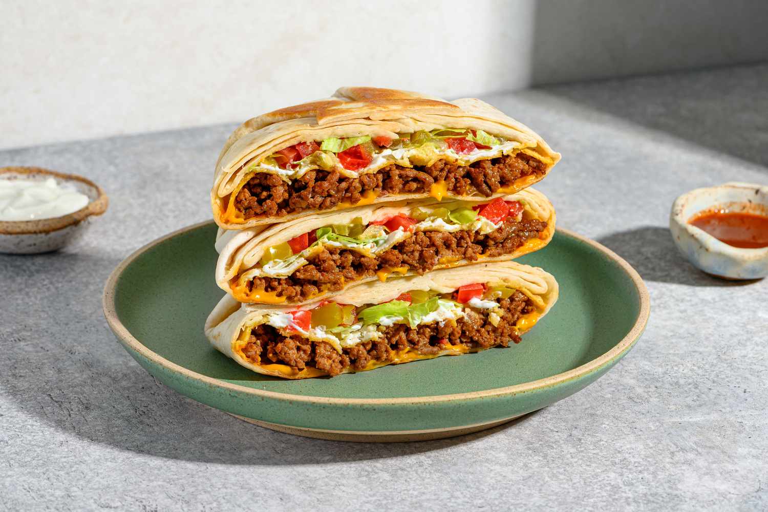 A golden-brown homemade Crunchwrap Supreme cut in half on a wooden board, showing layers of seasoned beef, melted nacho cheese, crunchy tostada, lettuce, and tomatoes in a bright home kitchen