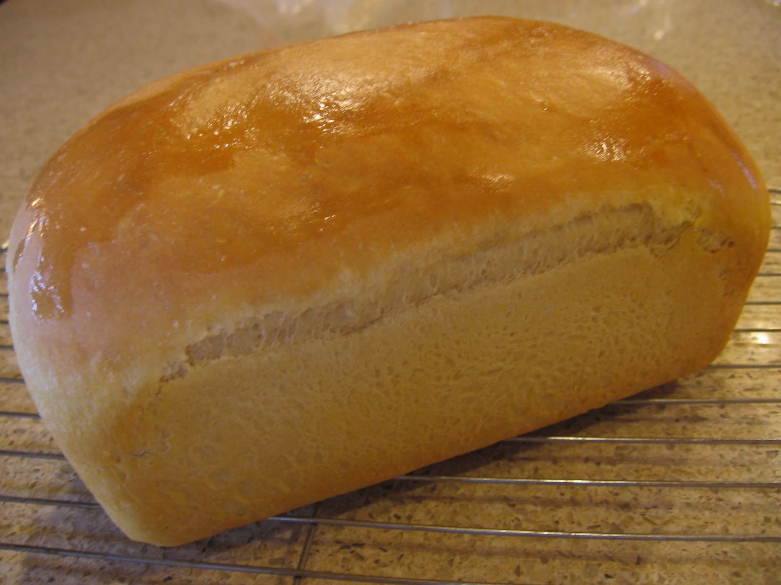 A golden brown homemade sandwich bread loaf cooling on a wooden cutting board on a bright kitchen counter