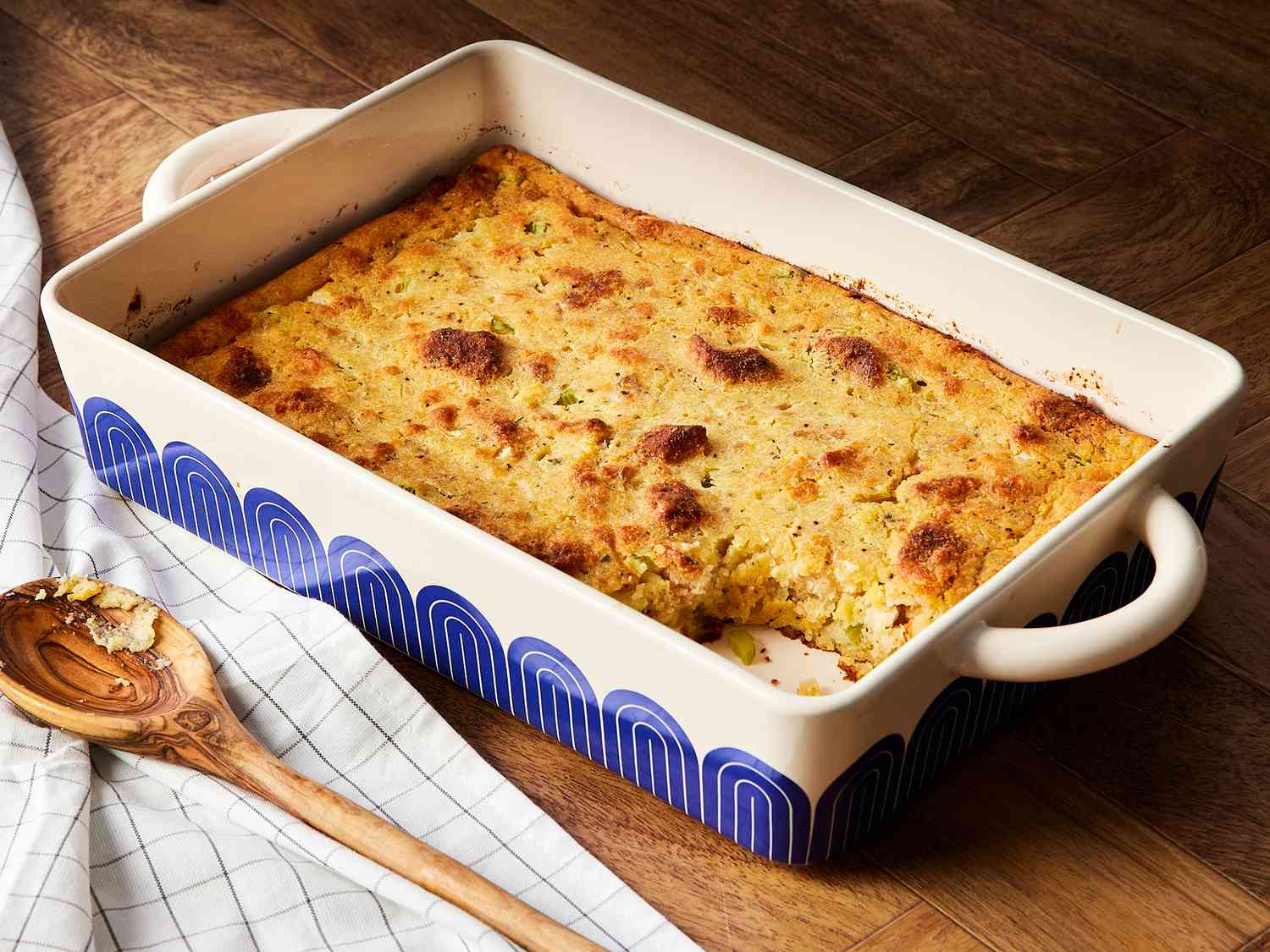 A golden brown pan of chicken dressing in a white ceramic baking dish on a warm kitchen counter, with crisp edges and a slightly crackled top