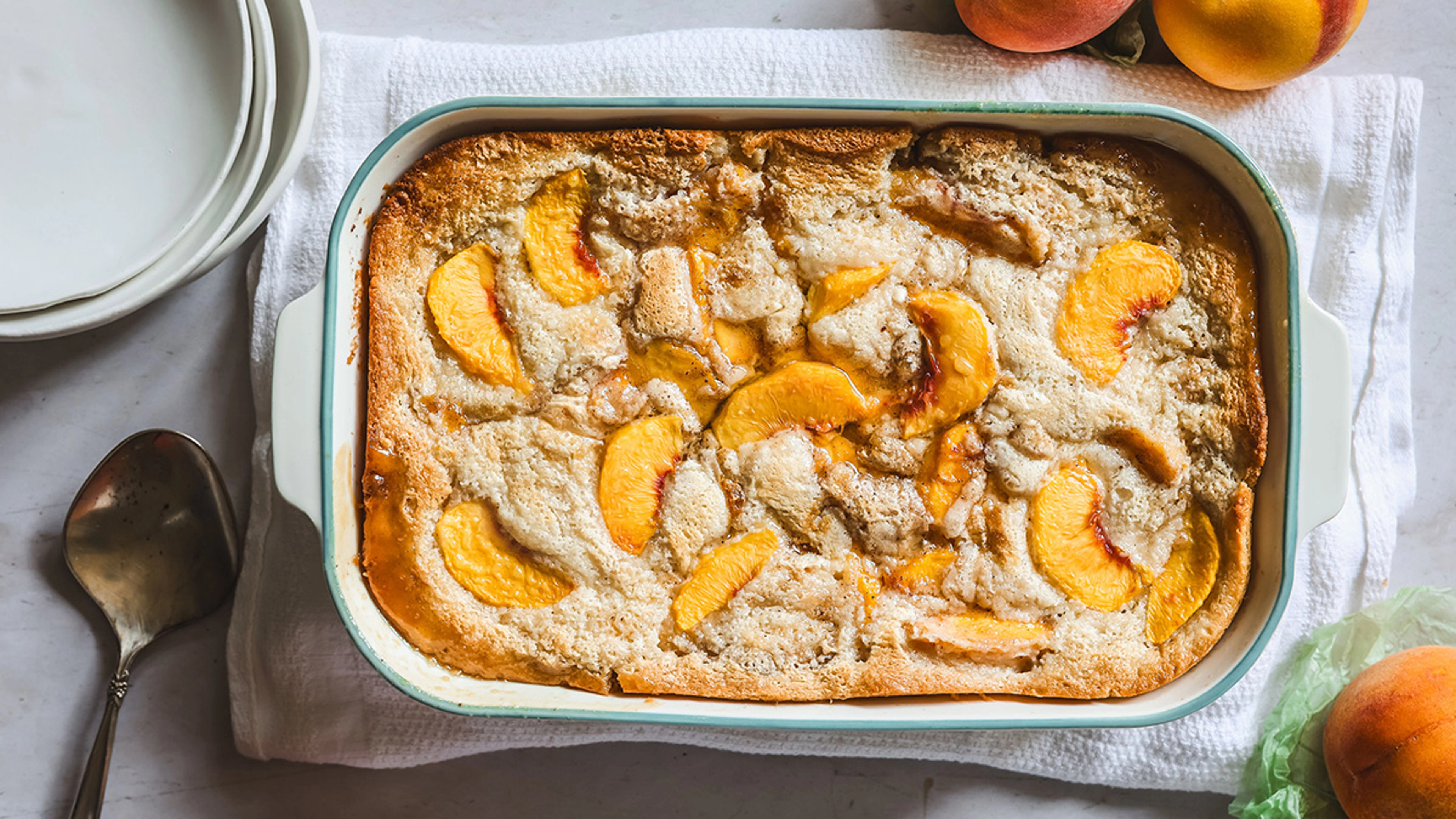 A golden brown peach cobbler in a rectangular baking dish with bubbling peach syrup around the edges on a kitchen counter