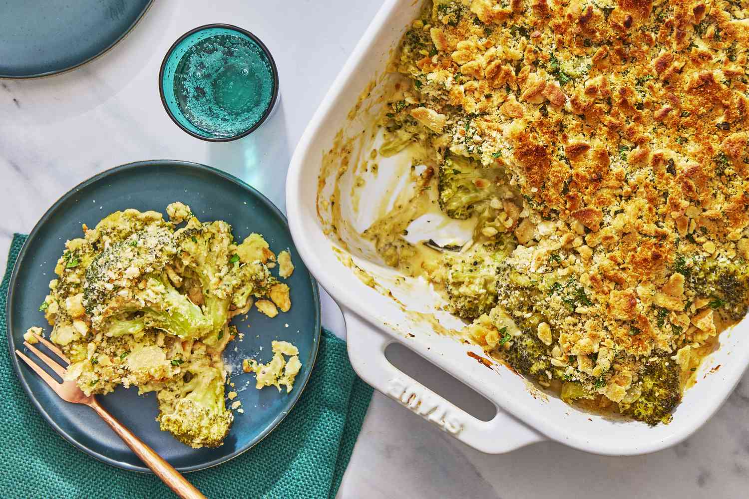 A golden, bubbly broccoli cheese casserole in a white ceramic baking dish on a bright kitchen counter, with a crisp cracker topping and a serving spoon nearby