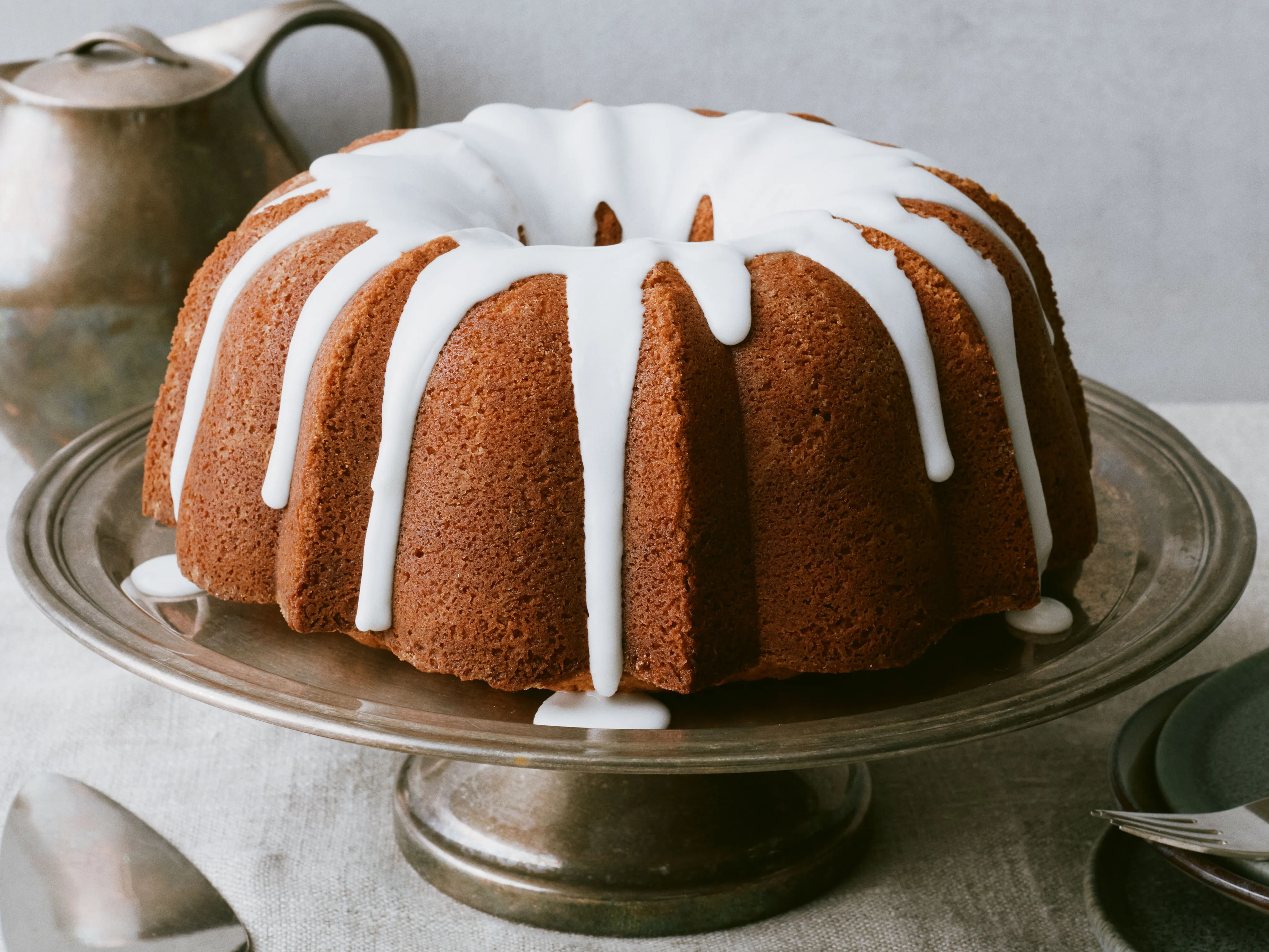 A golden bundt-style 7UP pound cake on a cake stand with a glossy lemon-lime glaze dripping down the sides on a bright kitchen counter