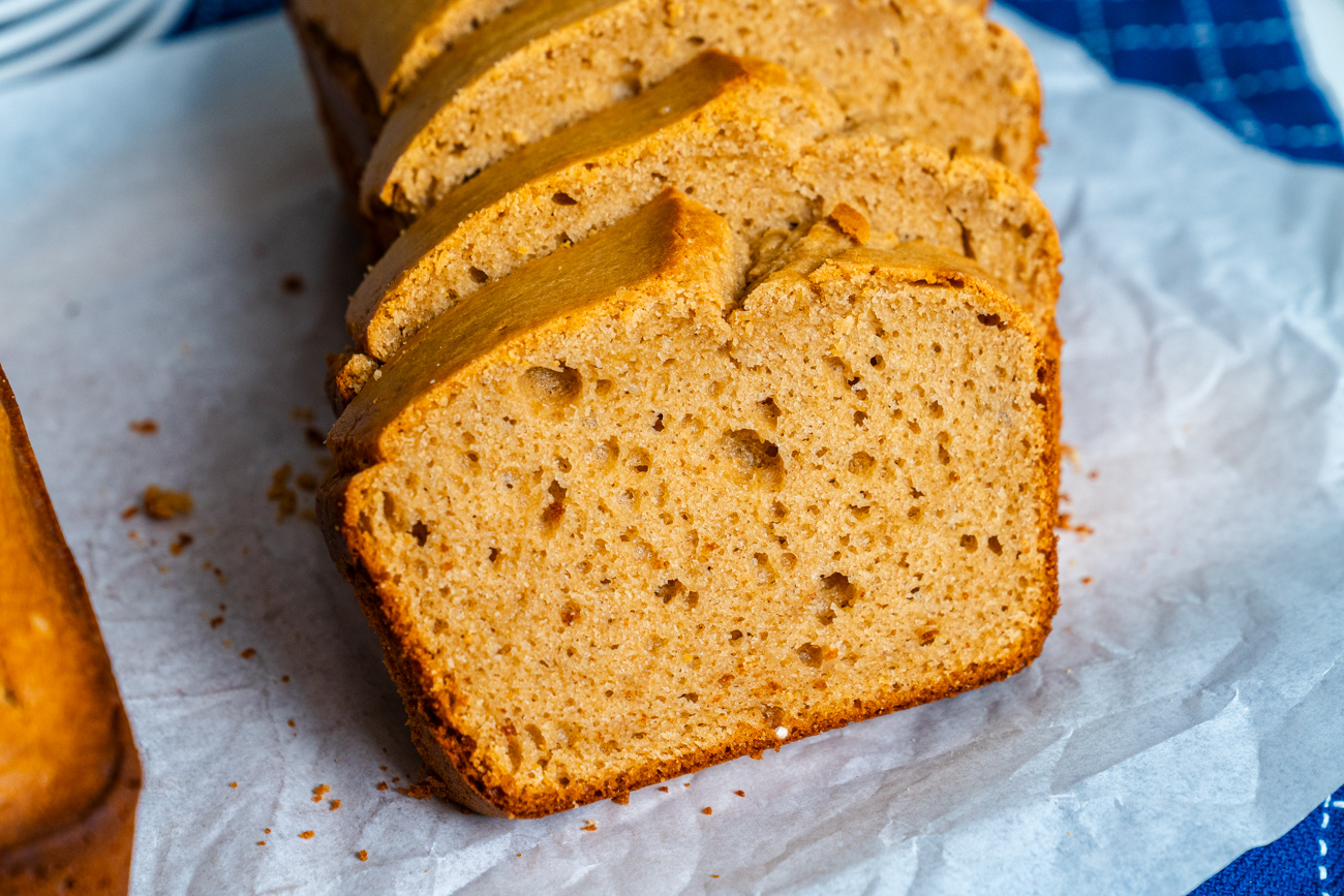 A golden loaf of peanut butter quick bread cooling on a wire rack on a warm kitchen counter, with a pat of butter melting on a sliced piece beside it