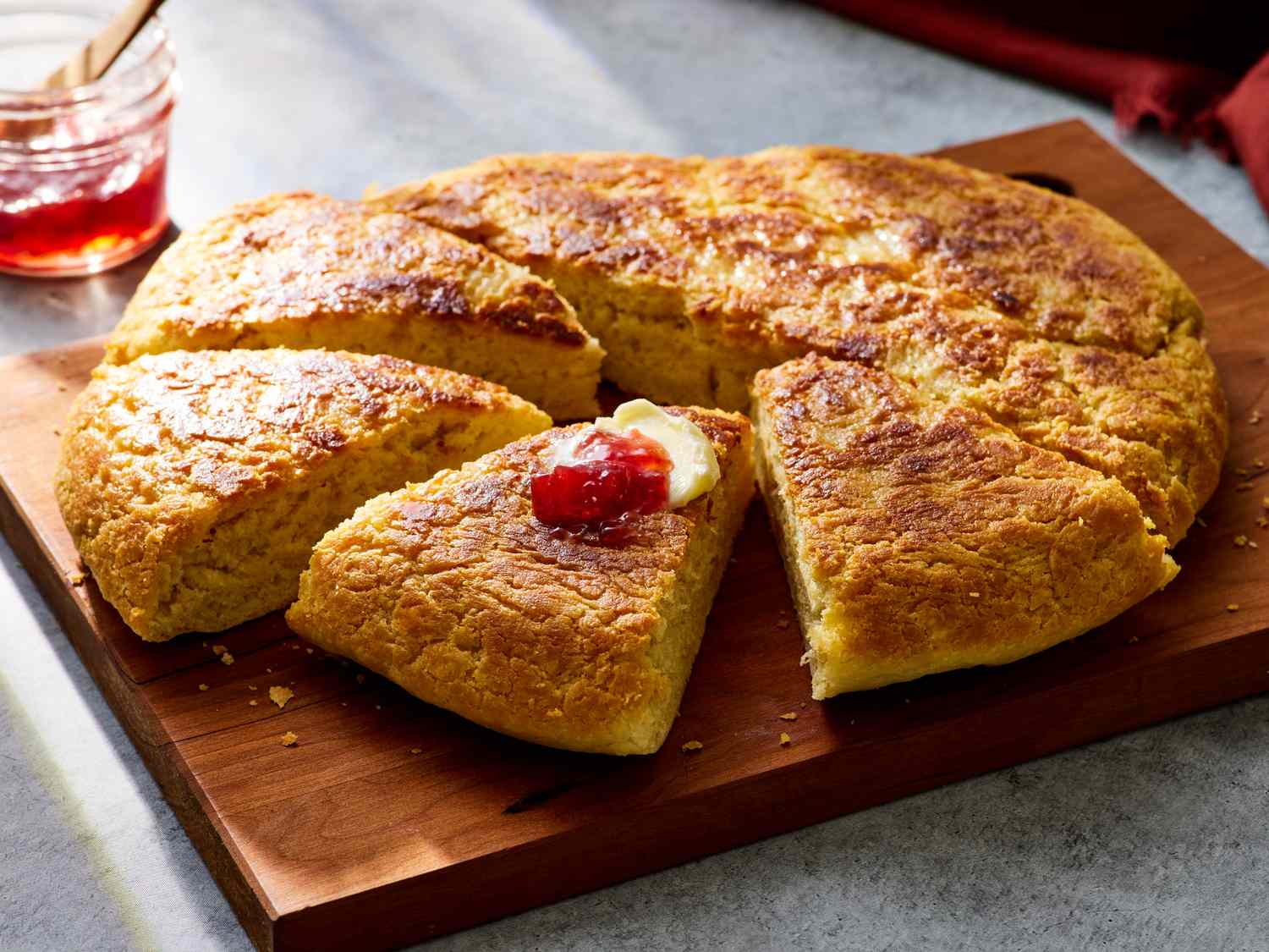 A golden round of skillet-cooked bannock cut into wedges on a wooden board with a small dish of butter, set on a cozy kitchen table with soft natural light