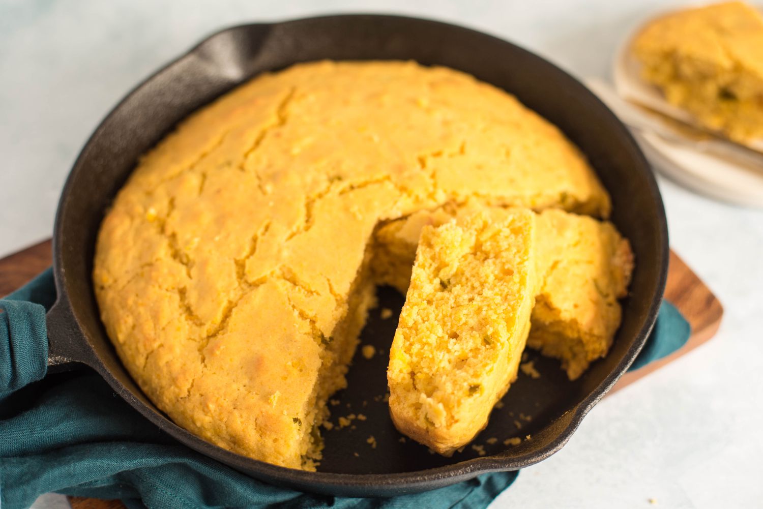 A golden vegan cornbread baked in a cast iron skillet on a rustic wooden table, with a single slice cut out showing a tender crumb