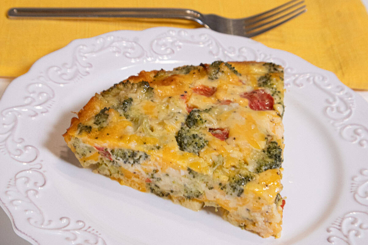 A golden vegetarian quiche lorraine slice on a ceramic plate with a flaky crust and browned top, set on a bright kitchen table with soft natural light